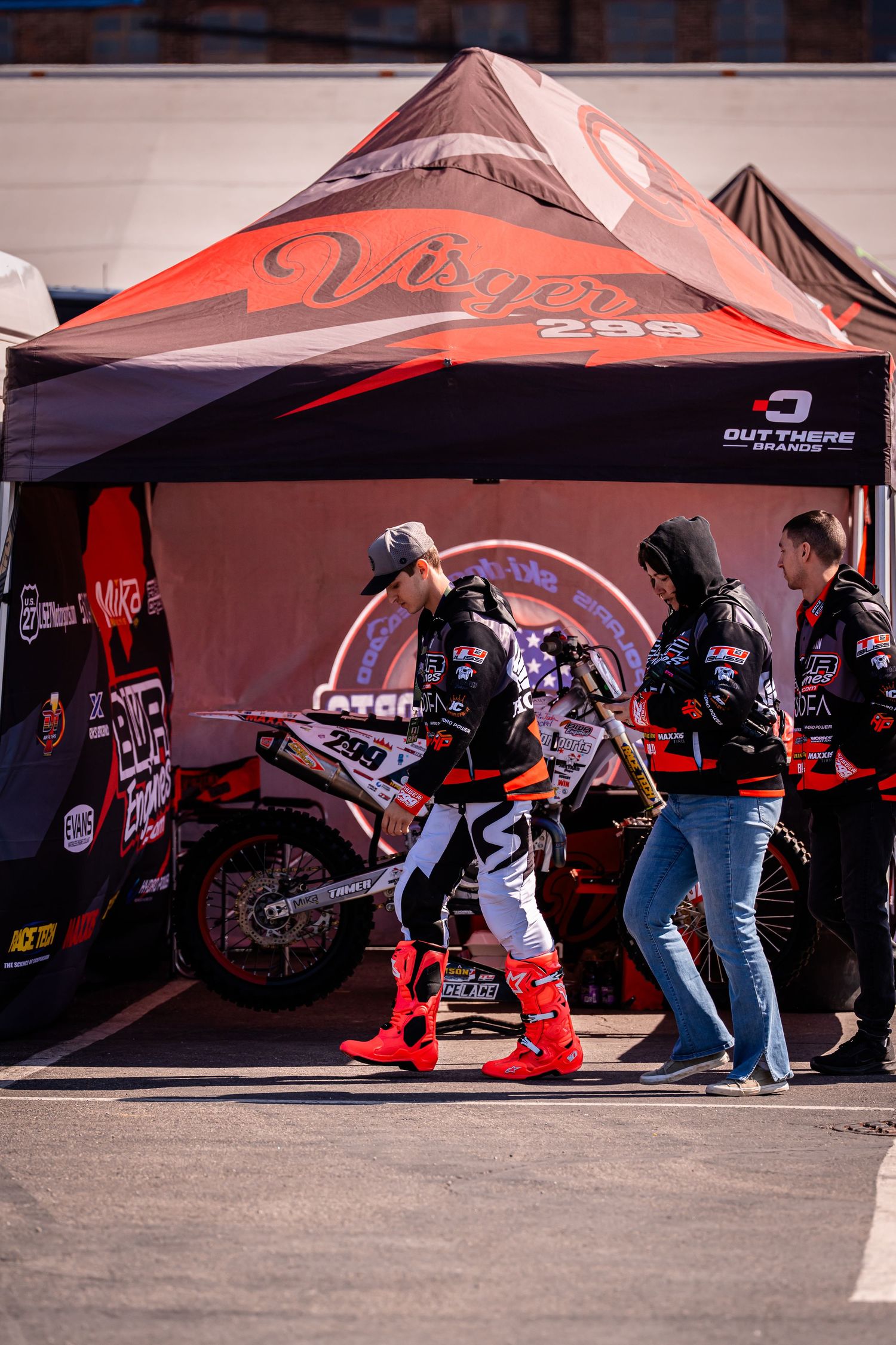 Dirt bike racing pit area with red canopy tents and crew members preparing for competition.