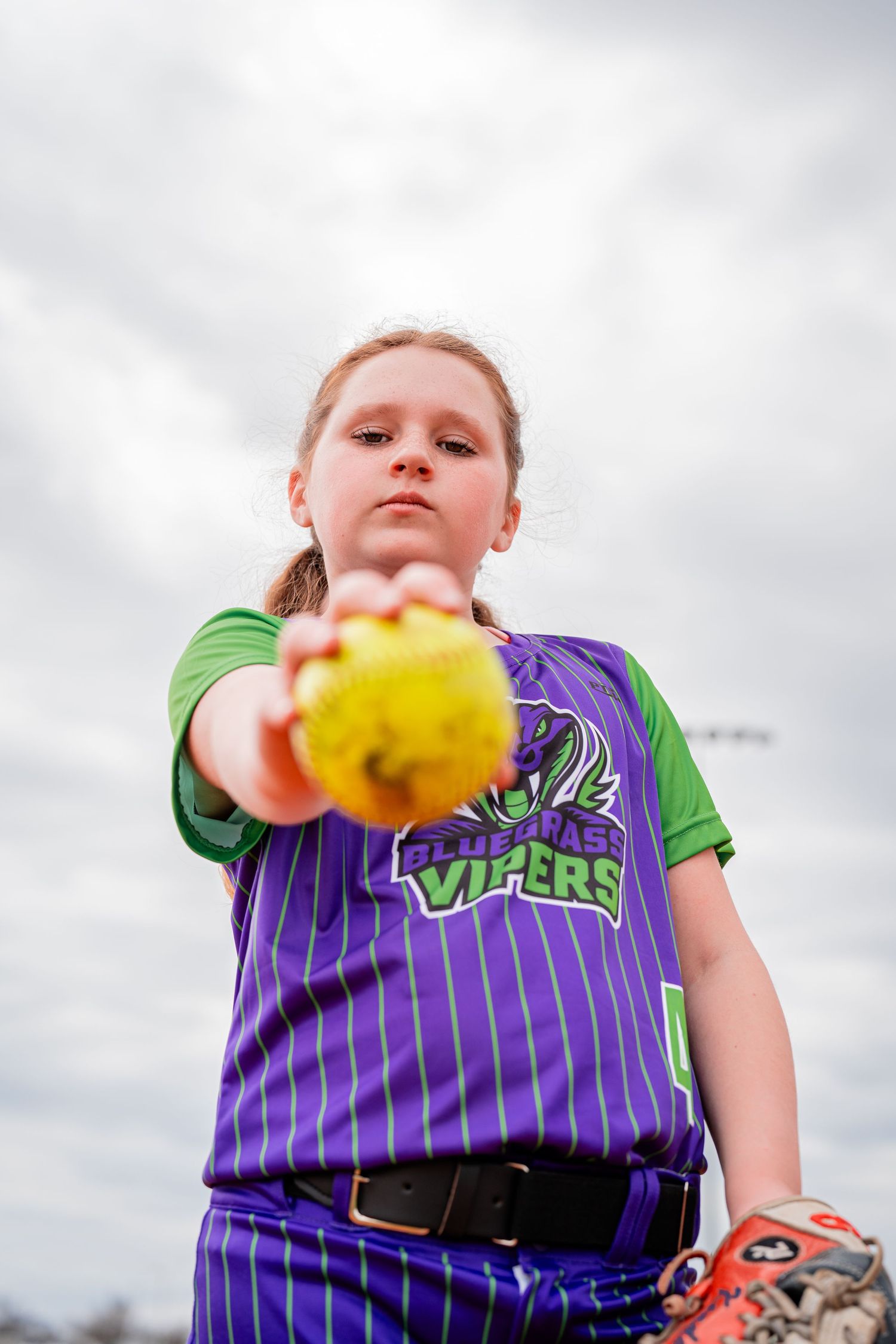 Softball player in Vipers uniform throws yellow ball during practice.