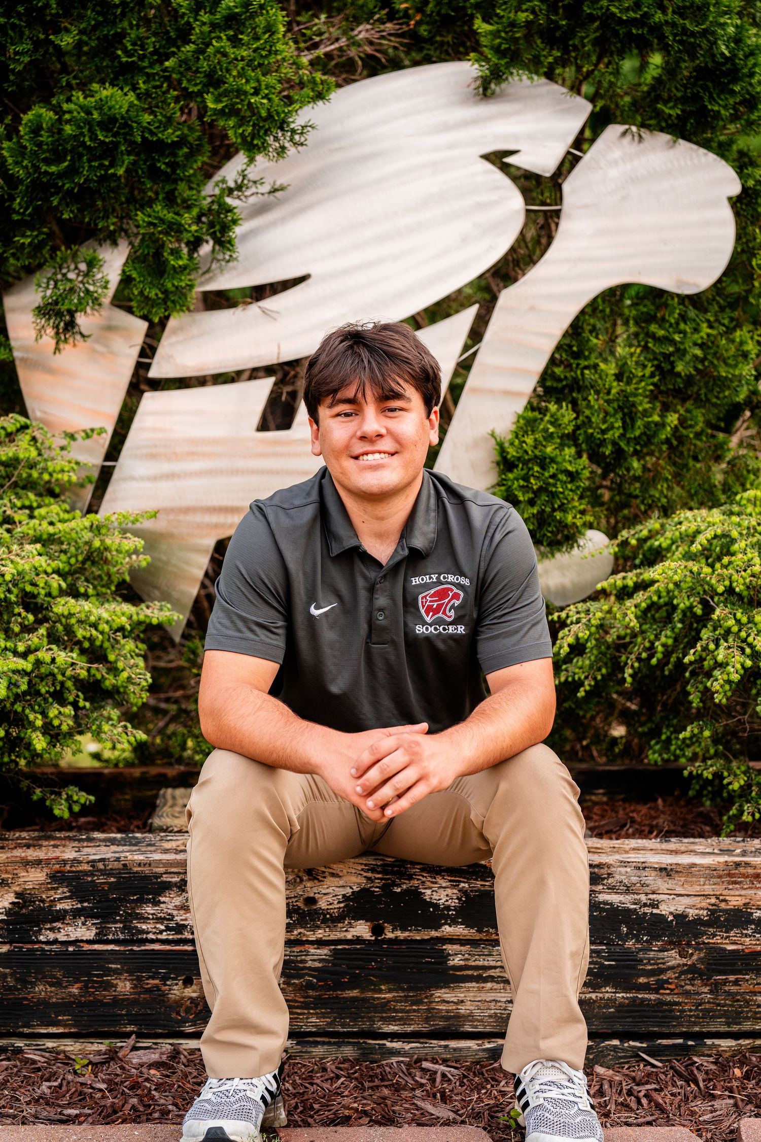Student athlete in Holy Cross gear sits on wooden bench for portrait.