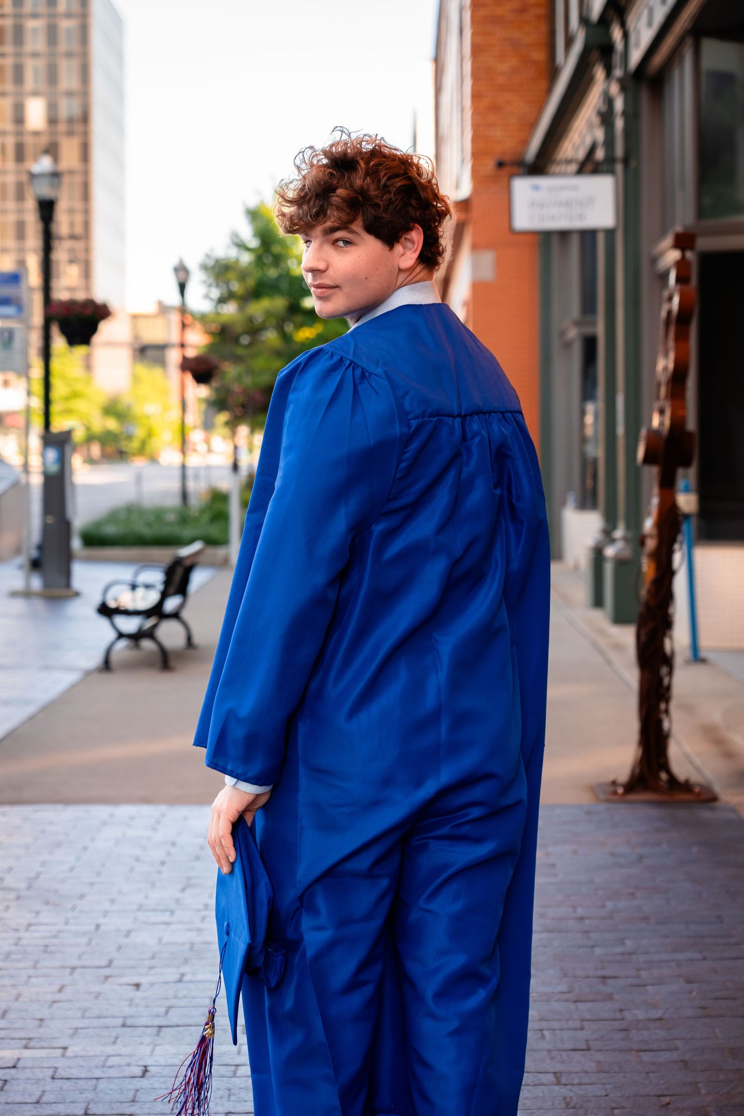 Person wearing graduation gown walking on brick sidewalk.