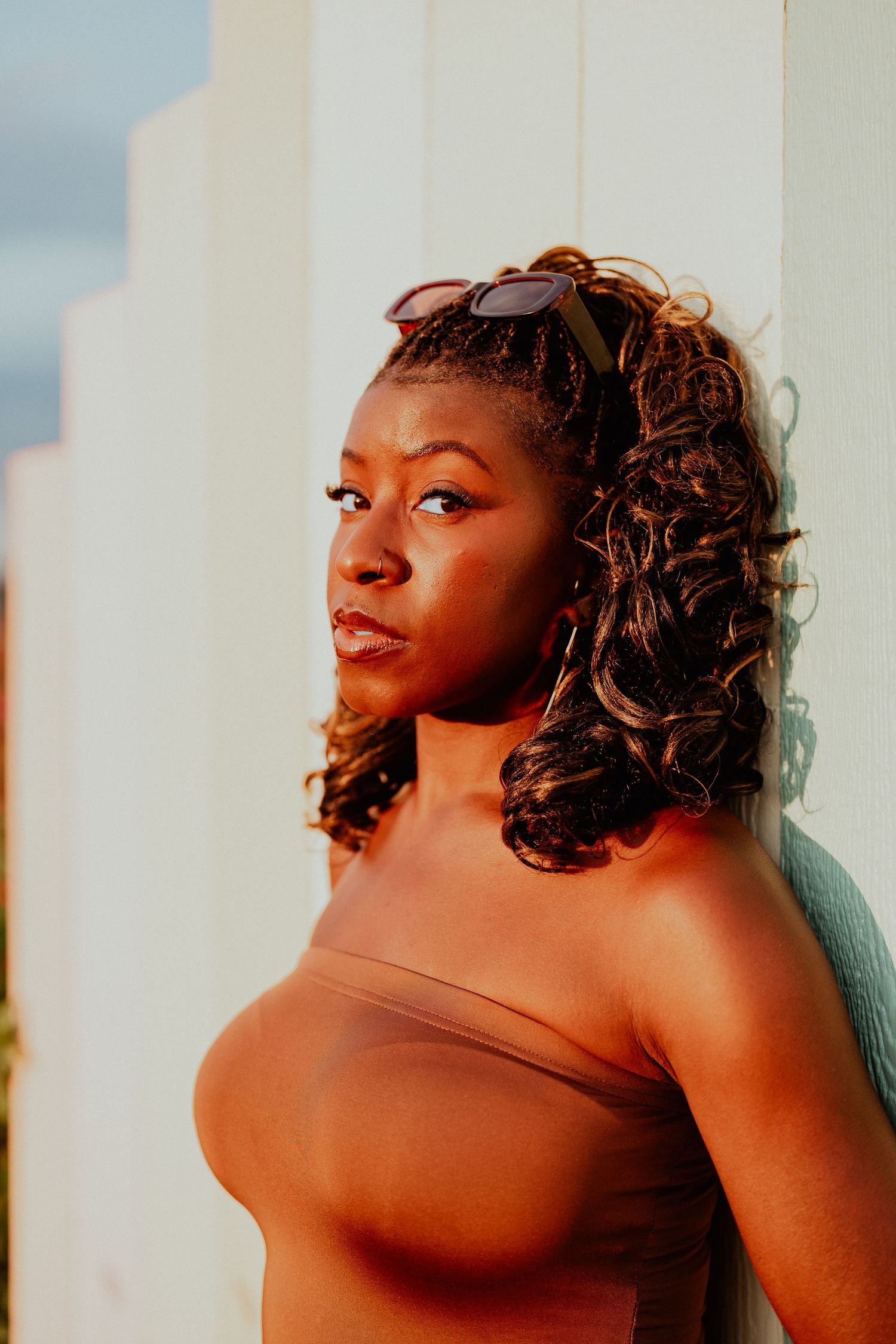 Artistic boudoir photoshoot with warm lighting and dramatic shadows against a light background.
