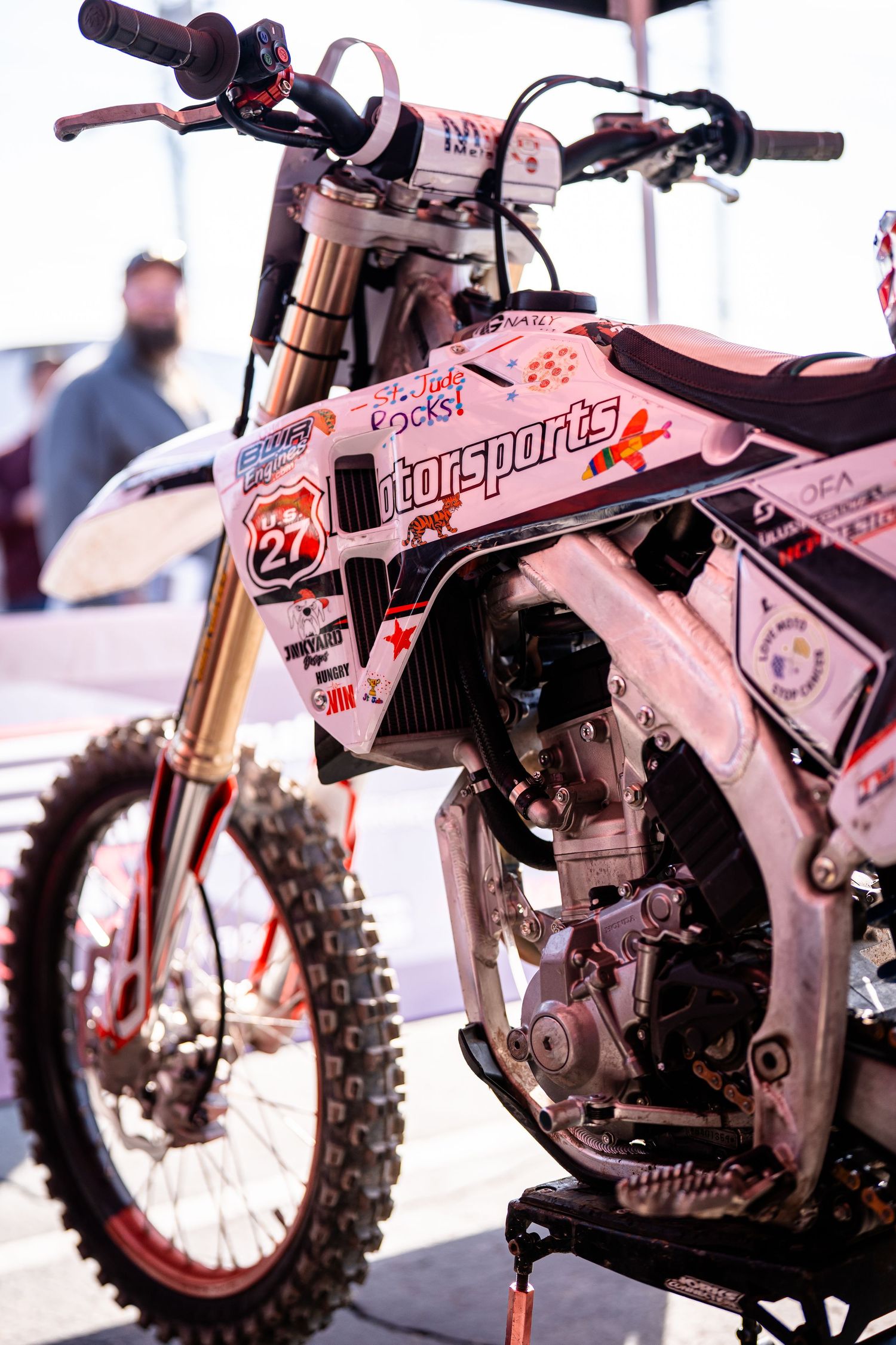 White dirt bike with racing modifications displayed at a motorsports show.
