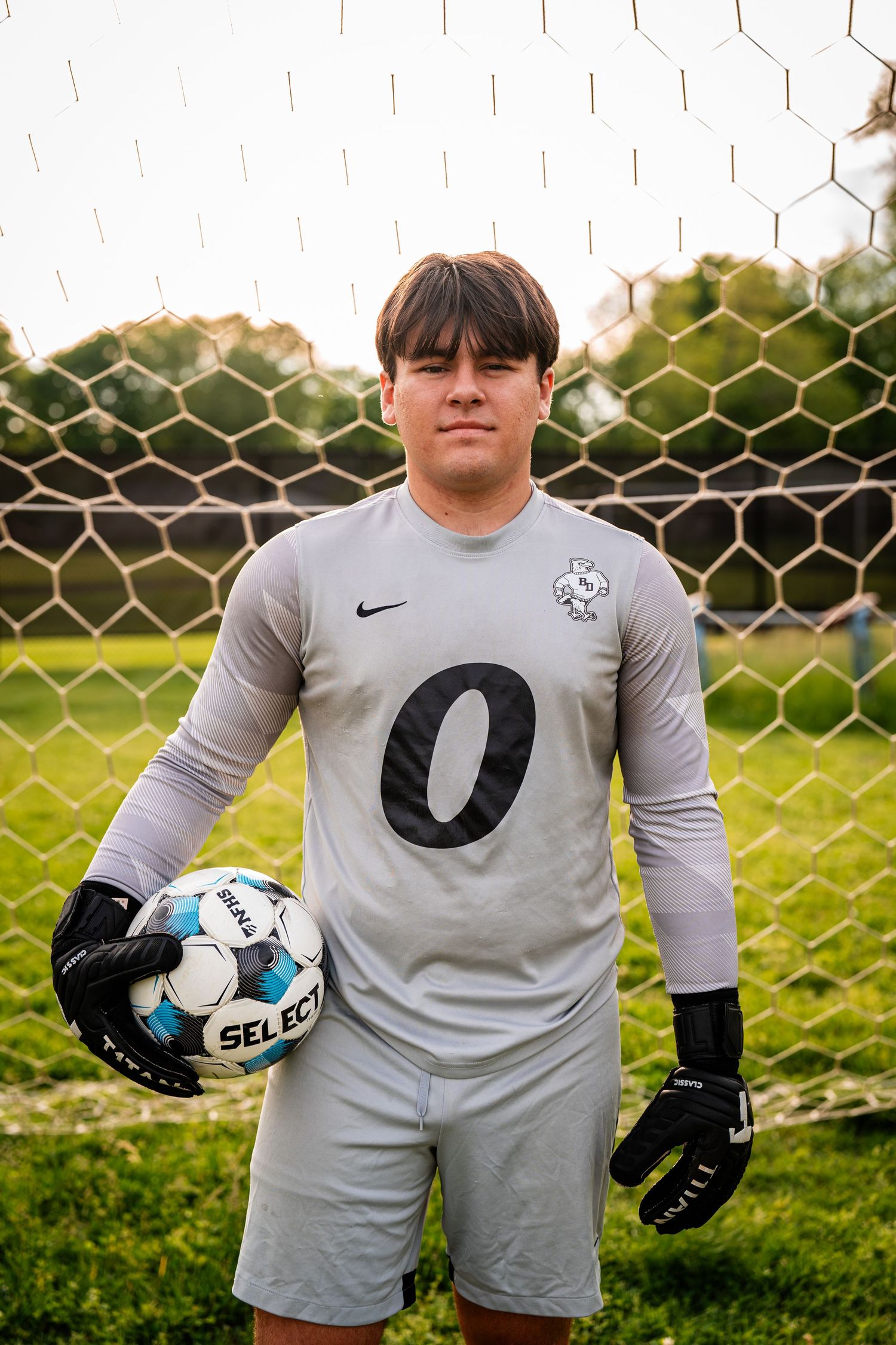 Soccer goalkeeper in gray jersey with gloves holds ball on field.