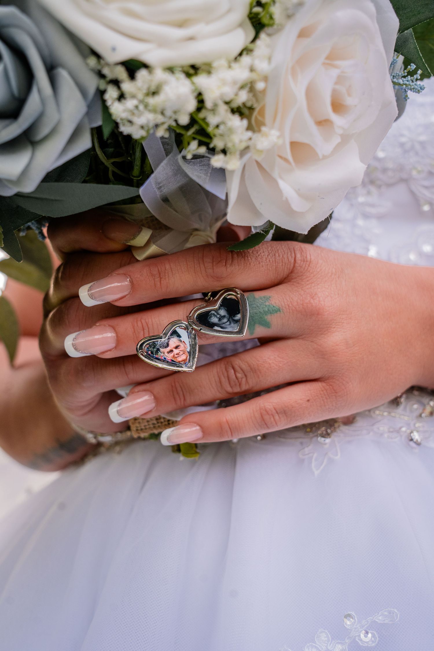 Close up of bride's hand with heart-shaped rings against white dress and floral bouquet.