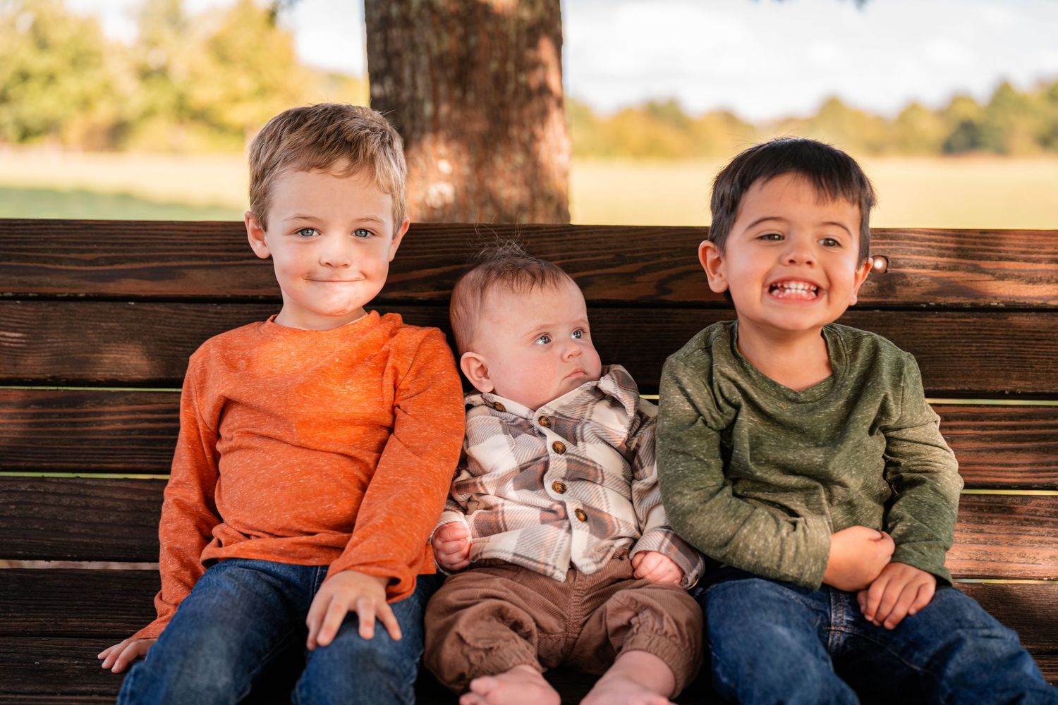 Three young children sitting together on a wooden bench outdoors.