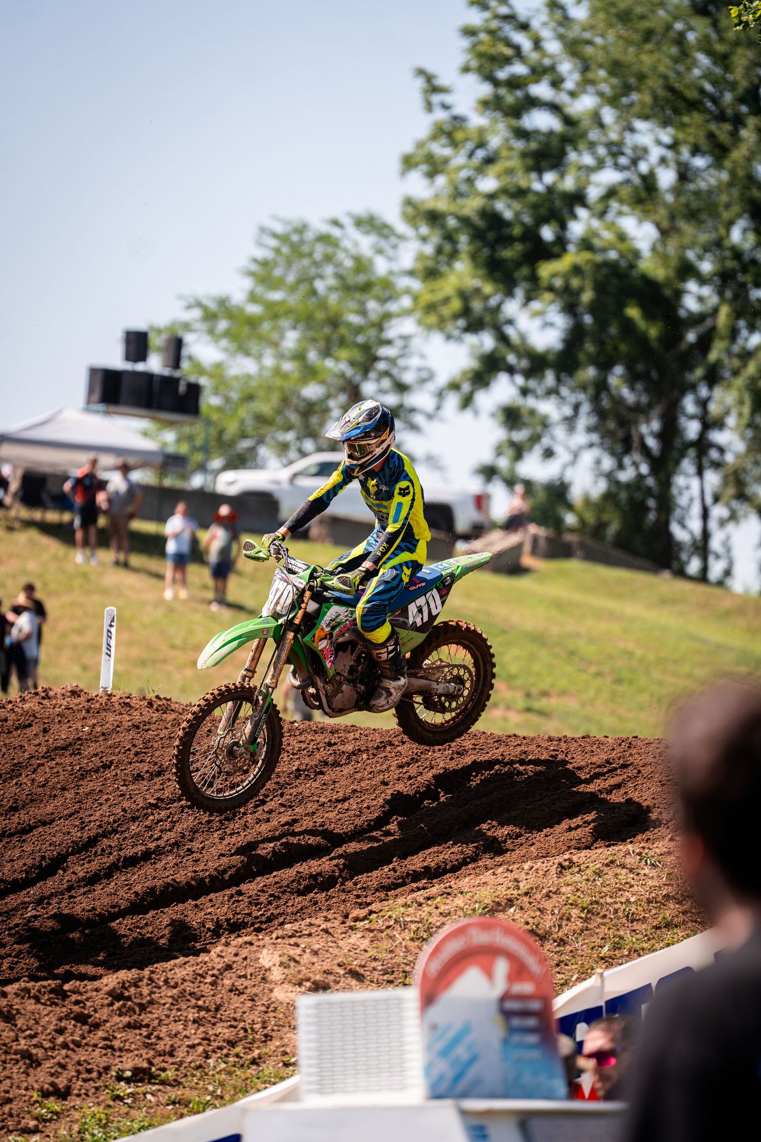 Dirt bike rider maneuvers through challenging motocross track with spectators watching from hillside.