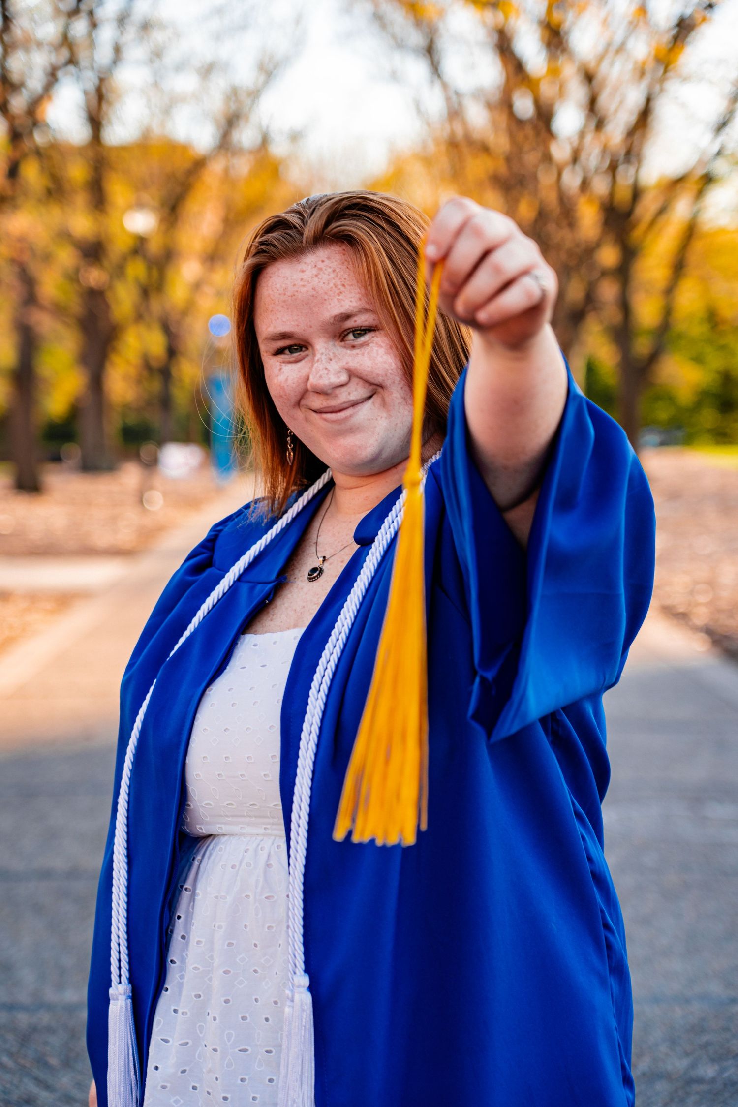Graduate holding yellow tassel from graduation cap during autumn ceremony.