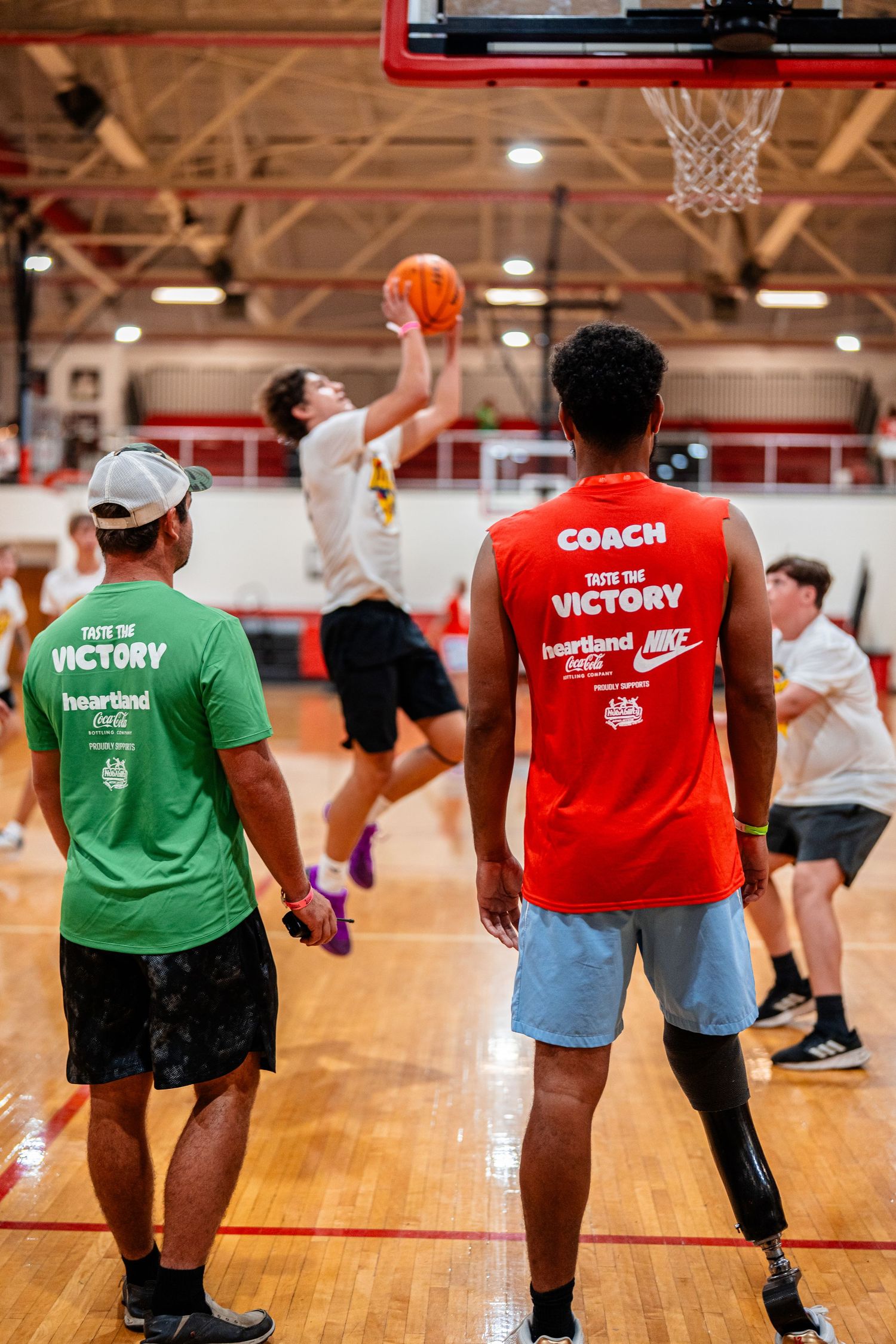 Athletes in colorful training shirts practice basketball drills in a gymnasium.