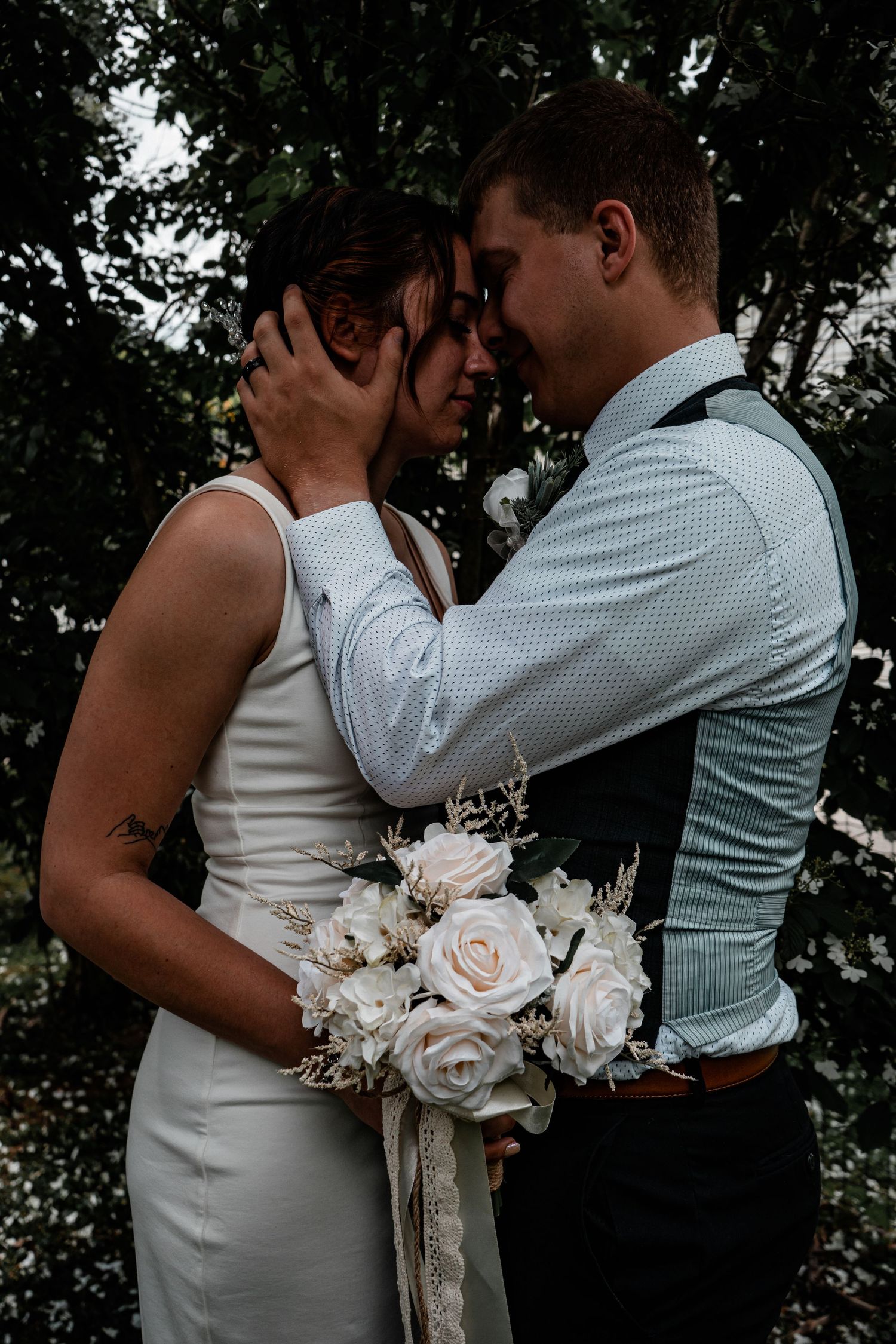 Romantic wedding portrait with bride holding white rose bouquet while embracing.