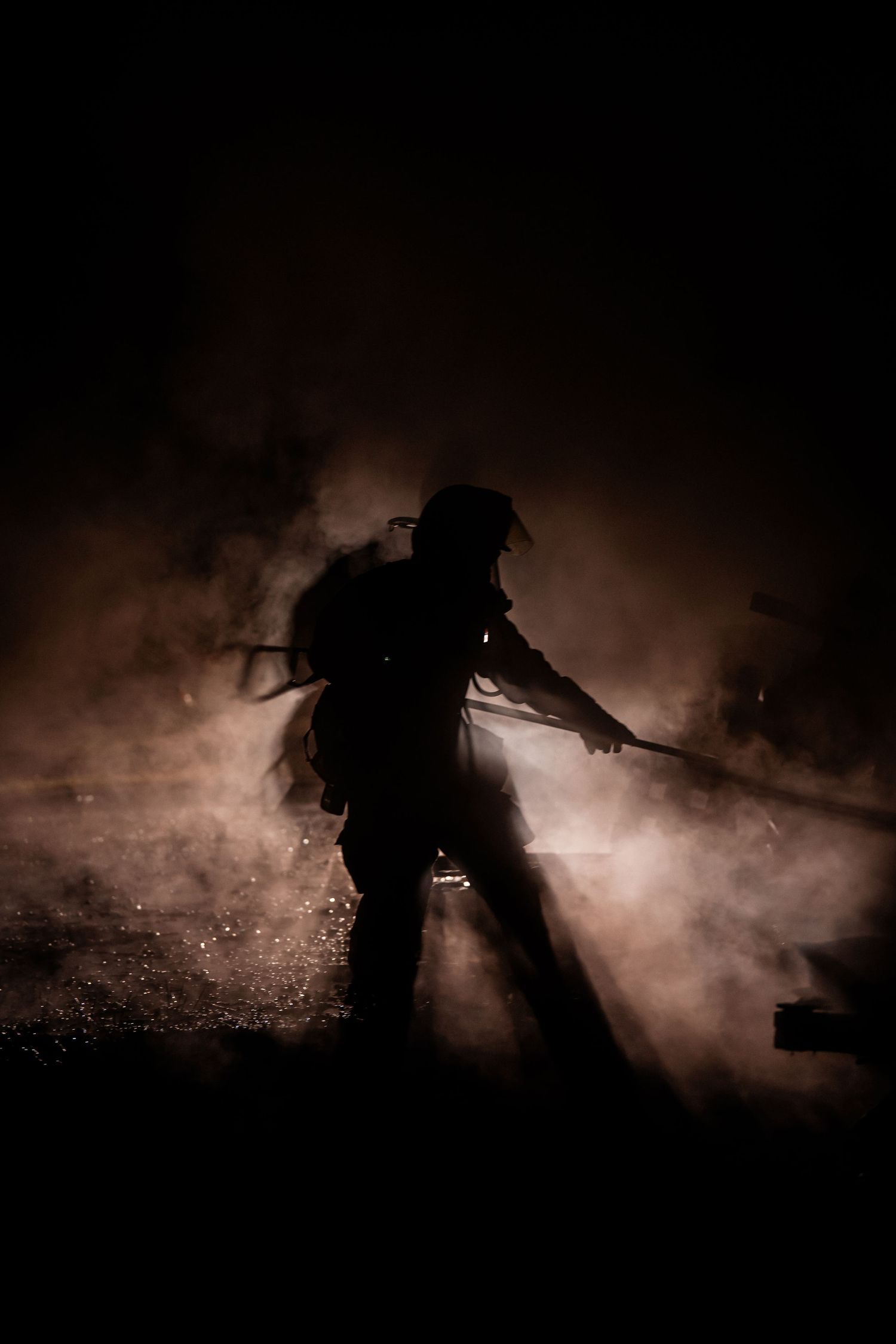 Atmospheric silhouettes of firefighters moving through smoke during a nighttime training exercise.