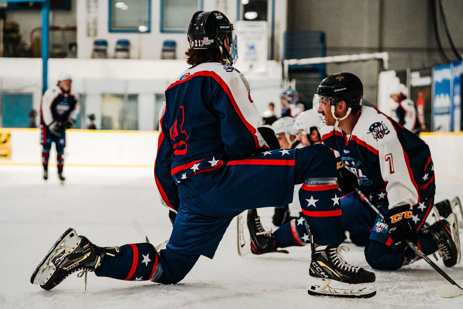 Hockey players in red and blue uniforms sliding on ice during game play.