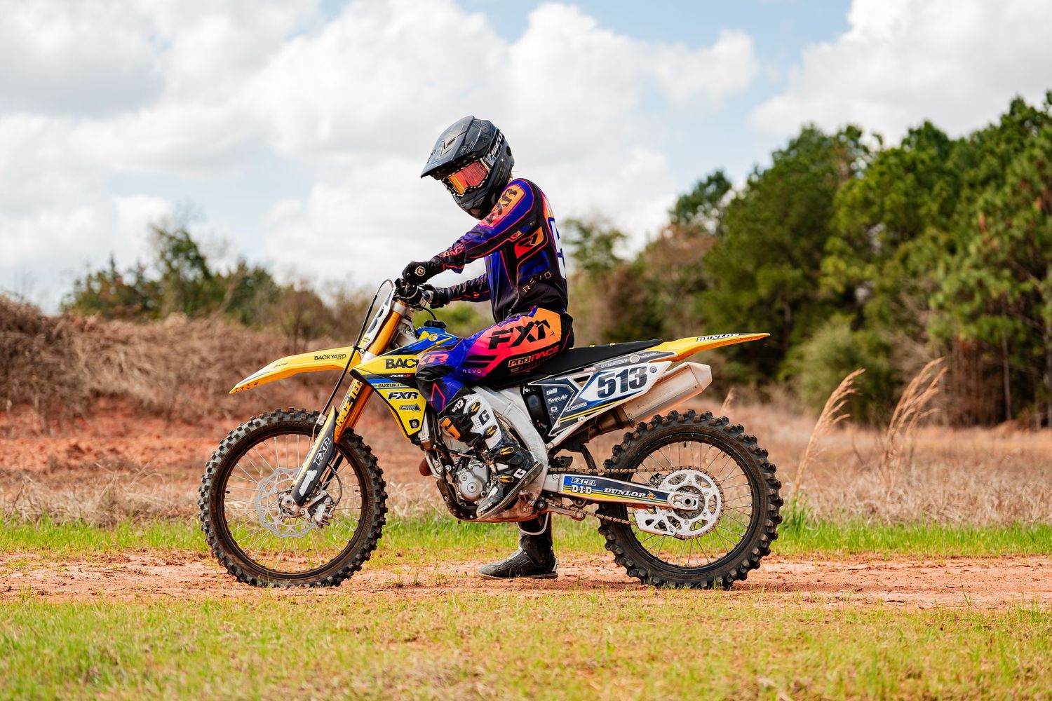 A person riding a dirt bike on a dusty track surrounded by trees and foliage.