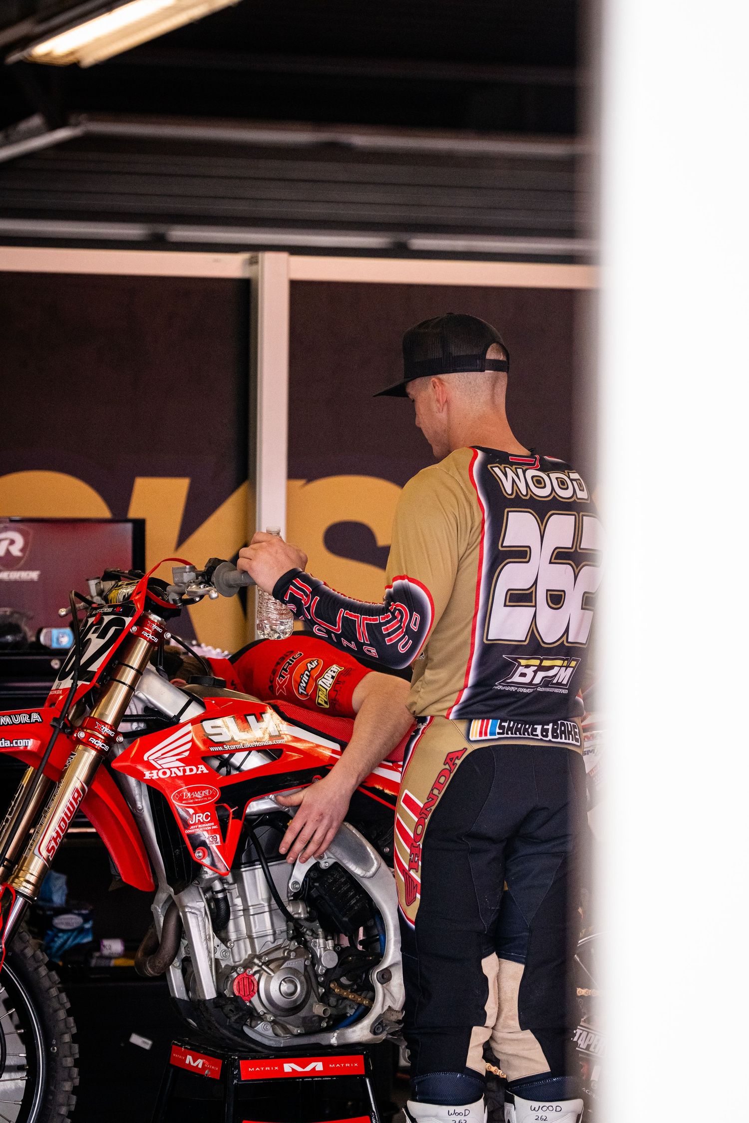 Mechanic works on red motocross bike in garage pit area.