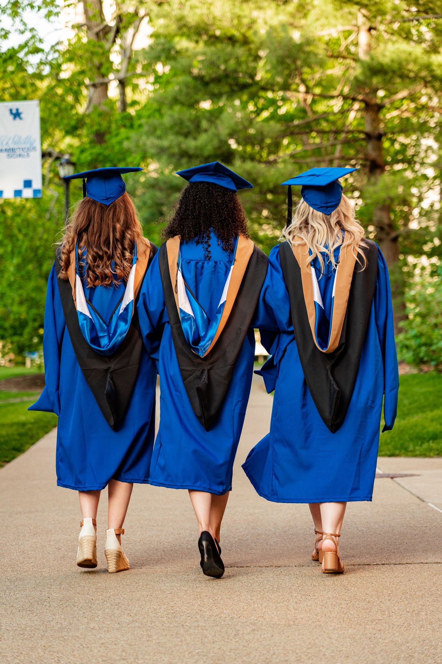Group of graduates in blue and black regalia walking together on campus path.