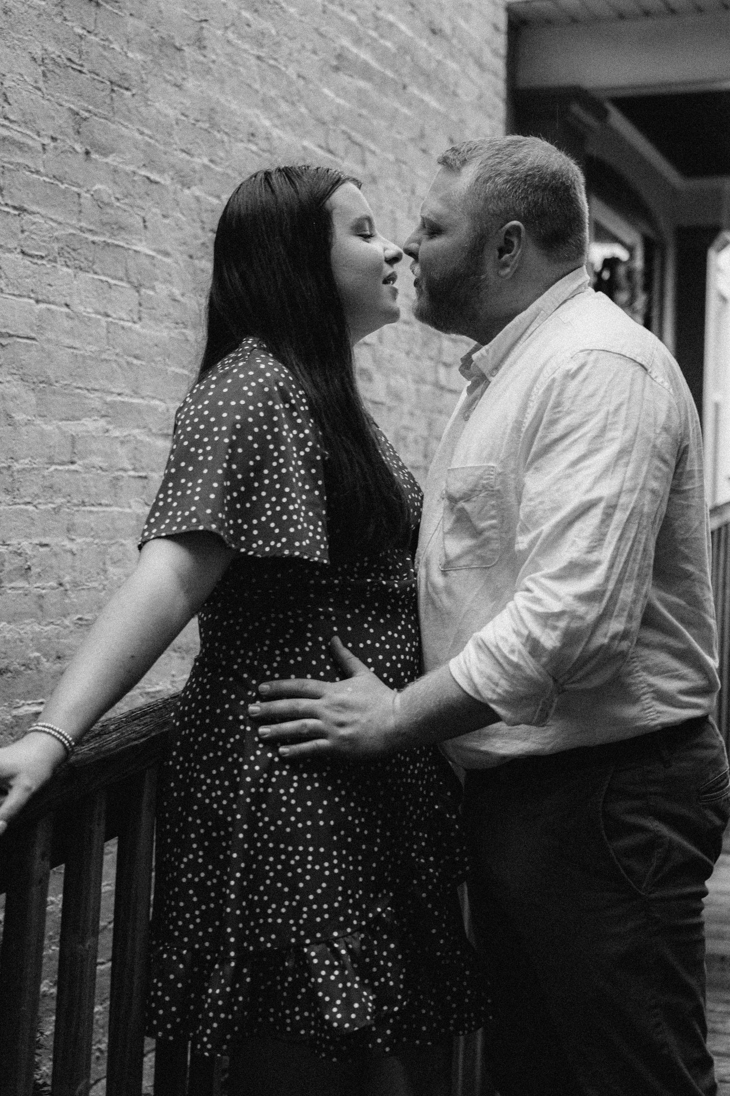An intimate black and white portrait against a brick wall background.