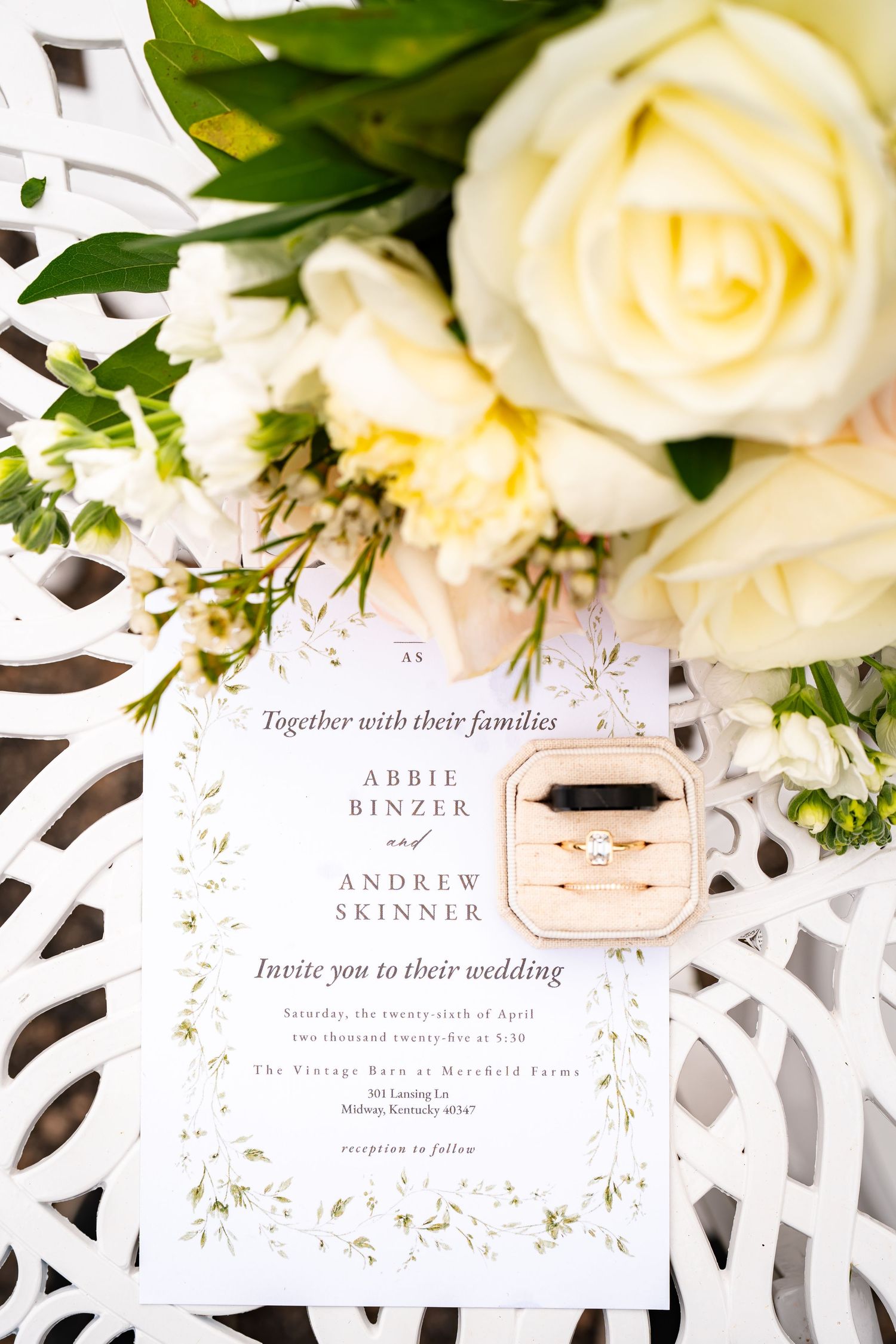 Elegant wedding invitation with white roses and floral details on lace background.