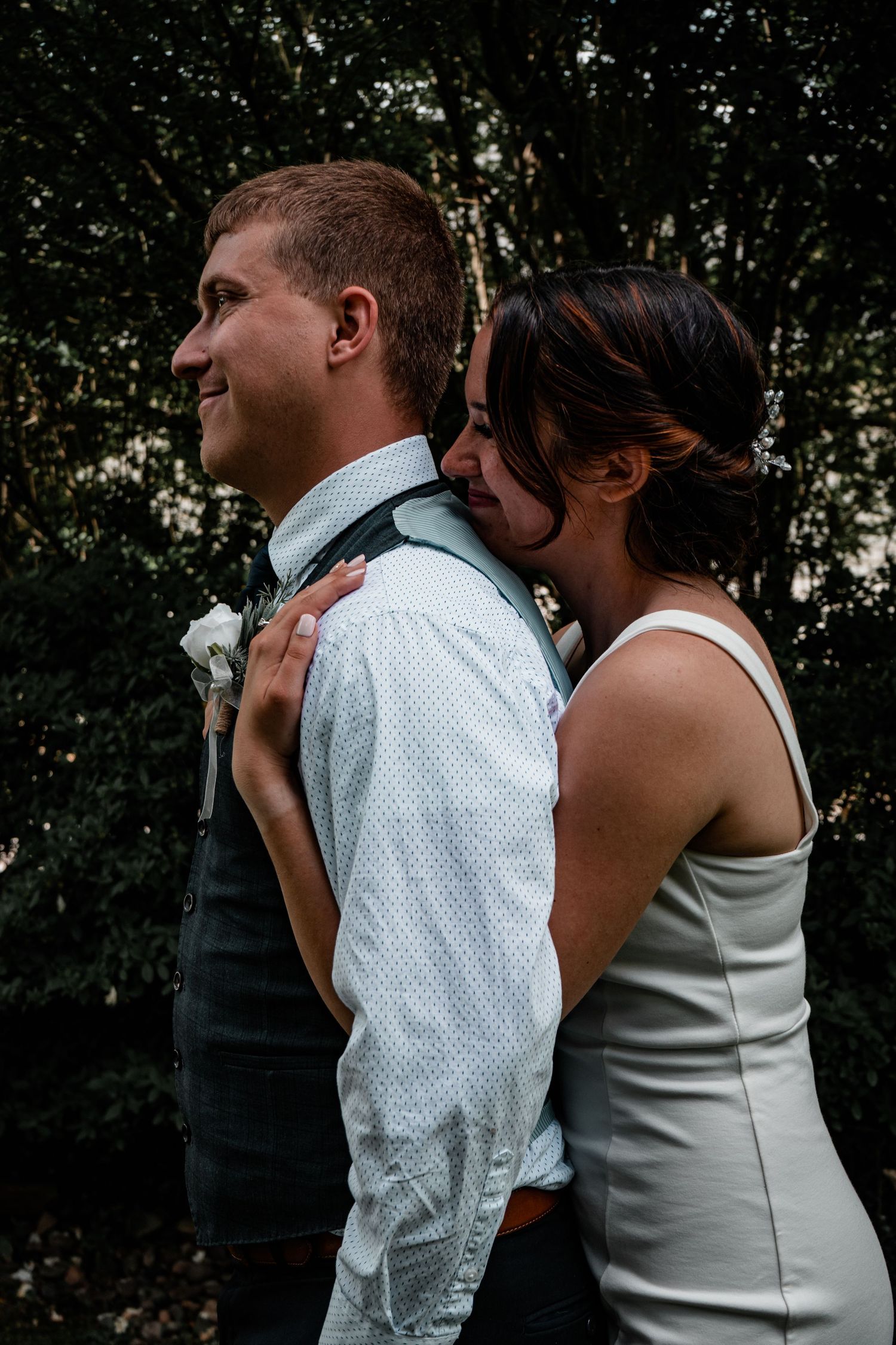 Intimate wedding moment captured between couple in formal attire against forest backdrop.