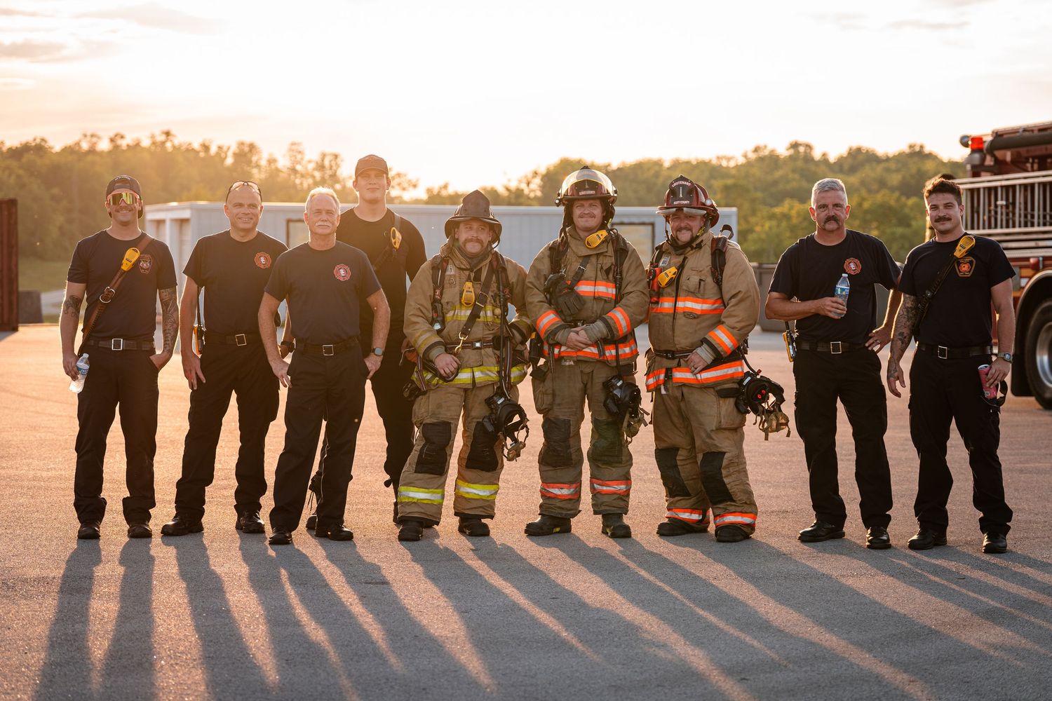 Silhouettes of firefighters lined up at sunset creating dramatic shadows on the ground.