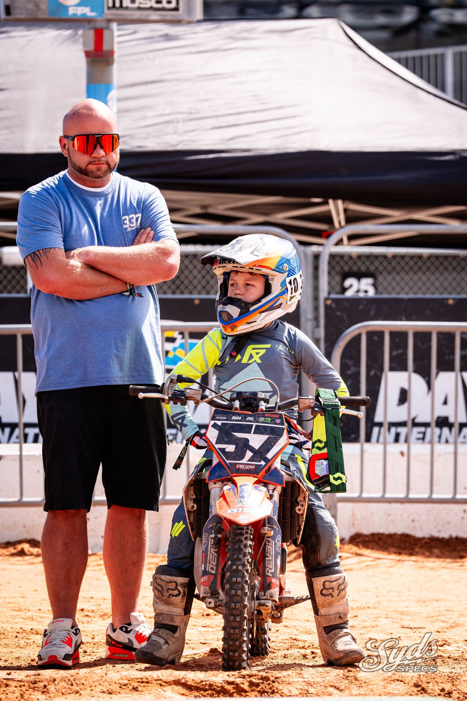 Young motocross rider on dirt bike with coach at racing event.