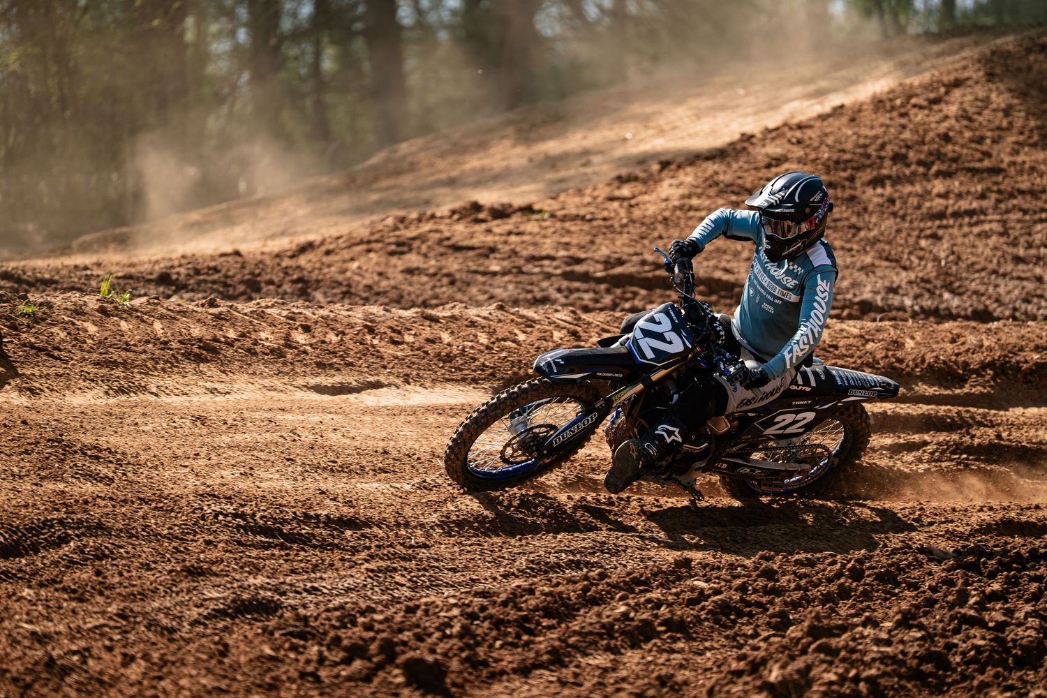 A motocross rider navigates a dirt track, kicking up dust as they lean into a turn on their motorcycle.