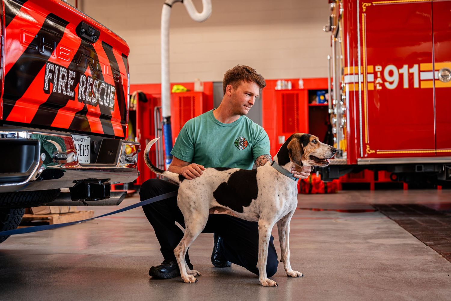 Dogs pose with handlers in front of bright red fire trucks in a station bay.