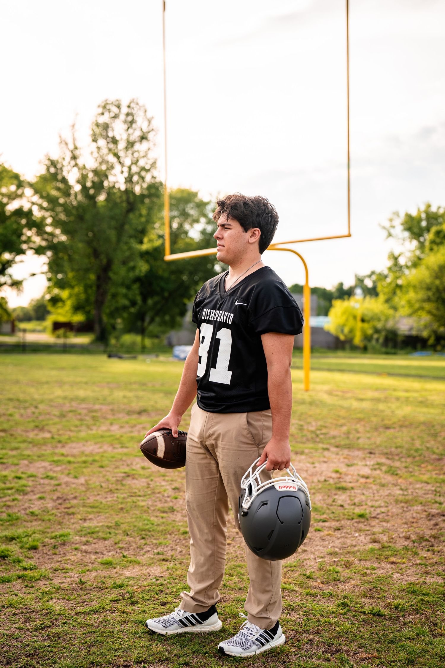Athlete in football gear poses with helmet on sports field at sunset.