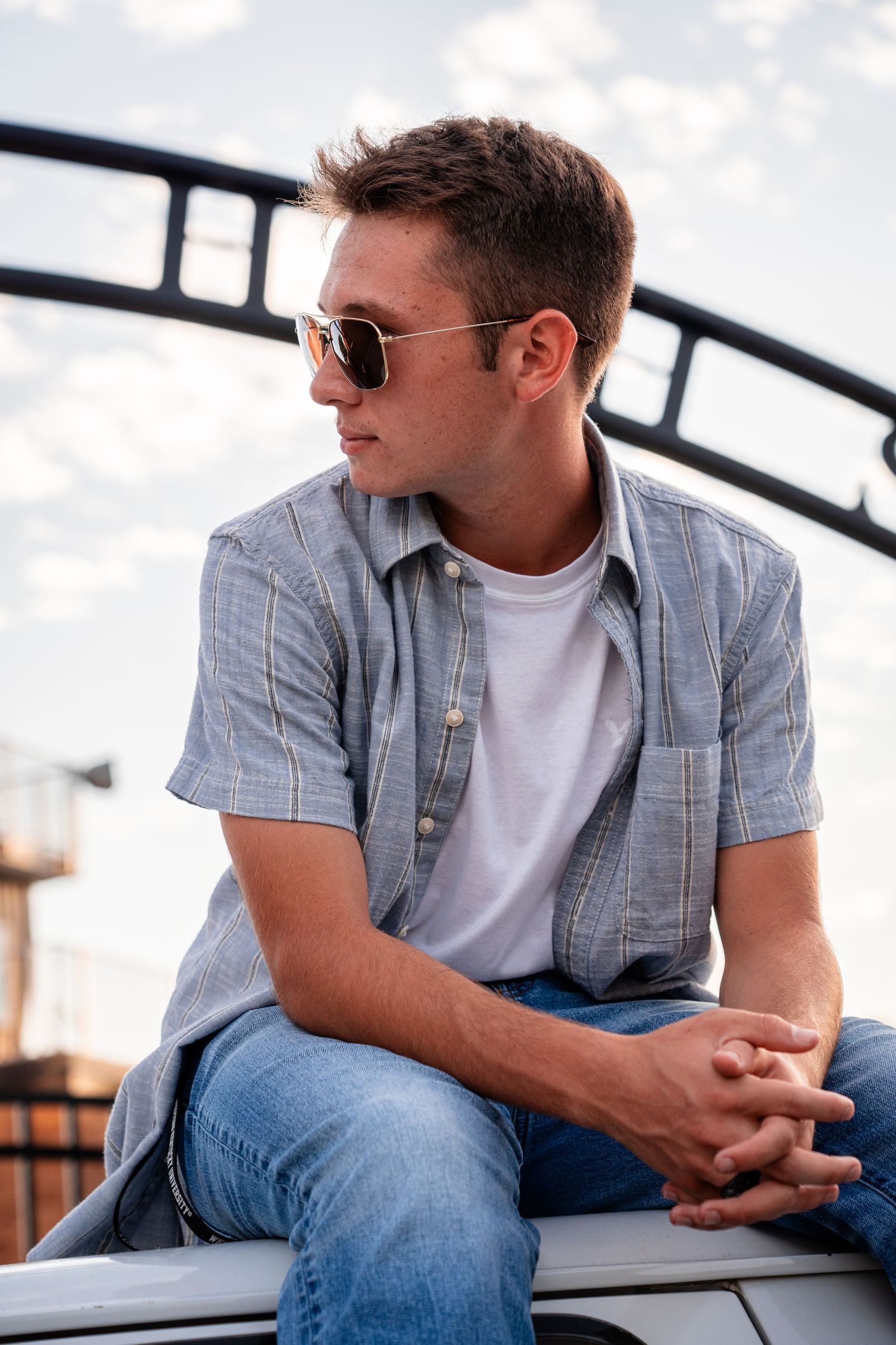Person in casual attire sitting on ledge wearing sunglasses.
