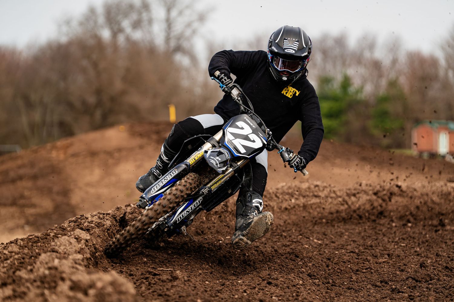A person riding a dirt bike on a muddy off-road track, kicking up dirt as they lean into the turn.