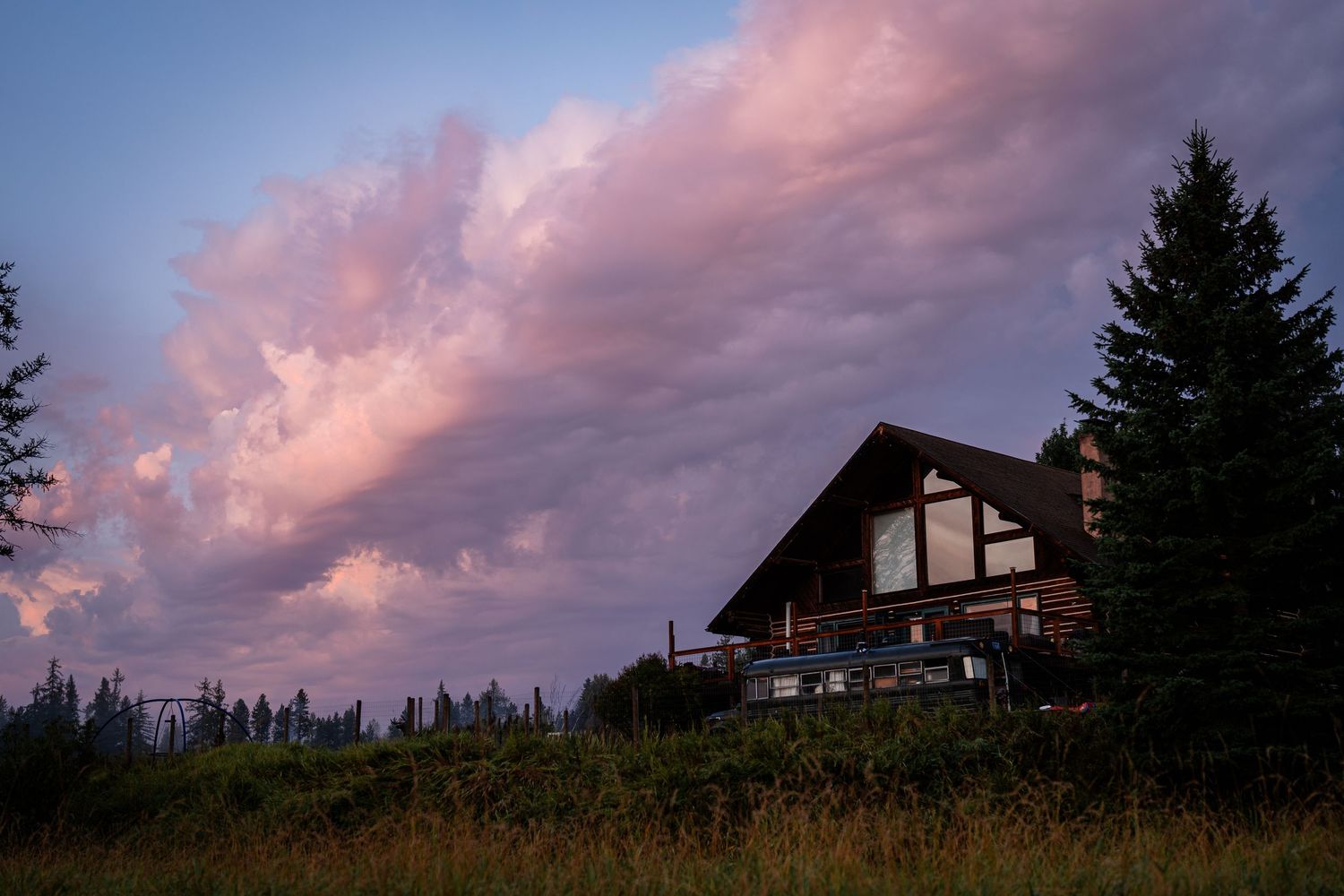 Dramatic pink sunset clouds over silhouetted mountain homes and trees.