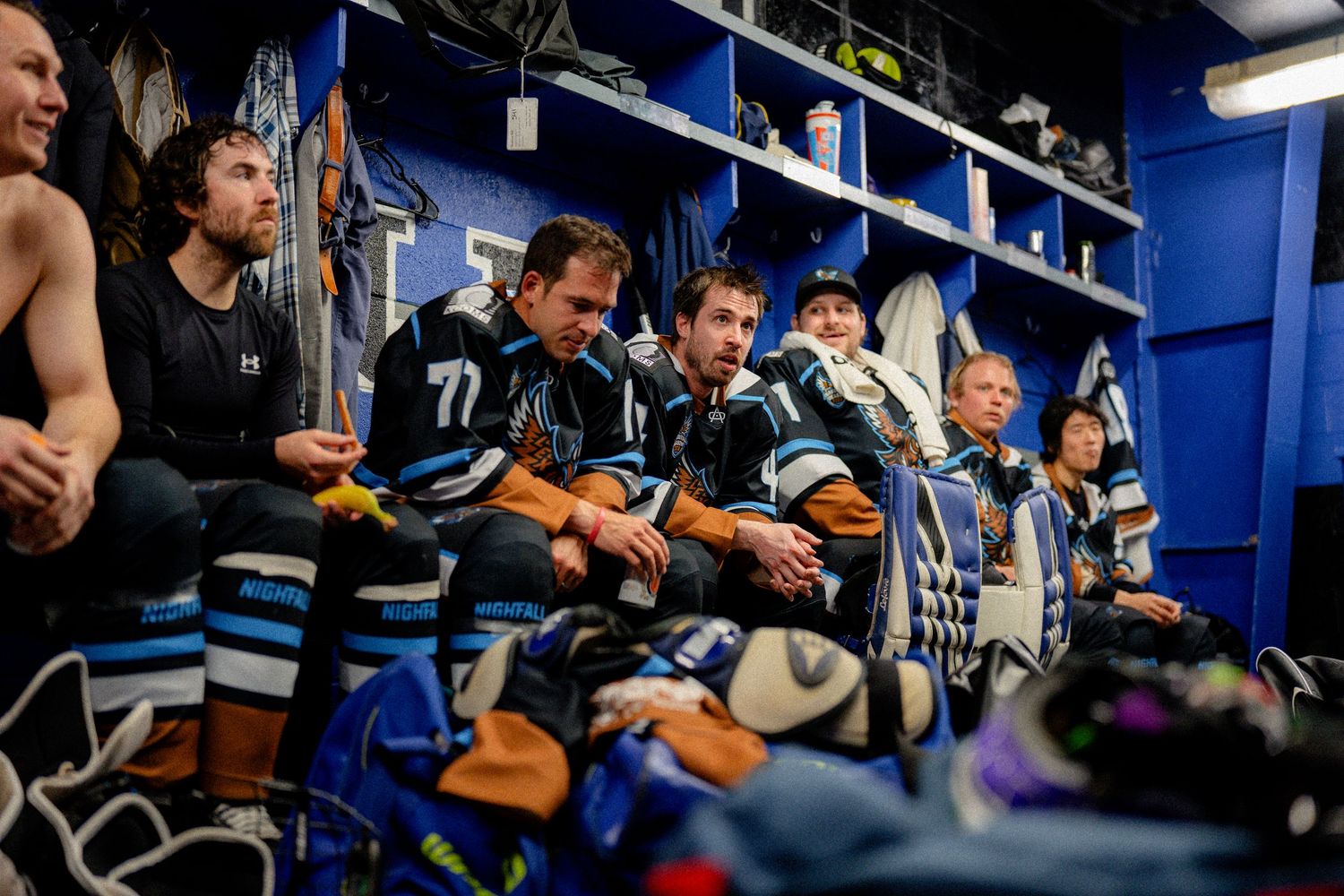 A group of hockey players sitting on a bench in a locker room.
