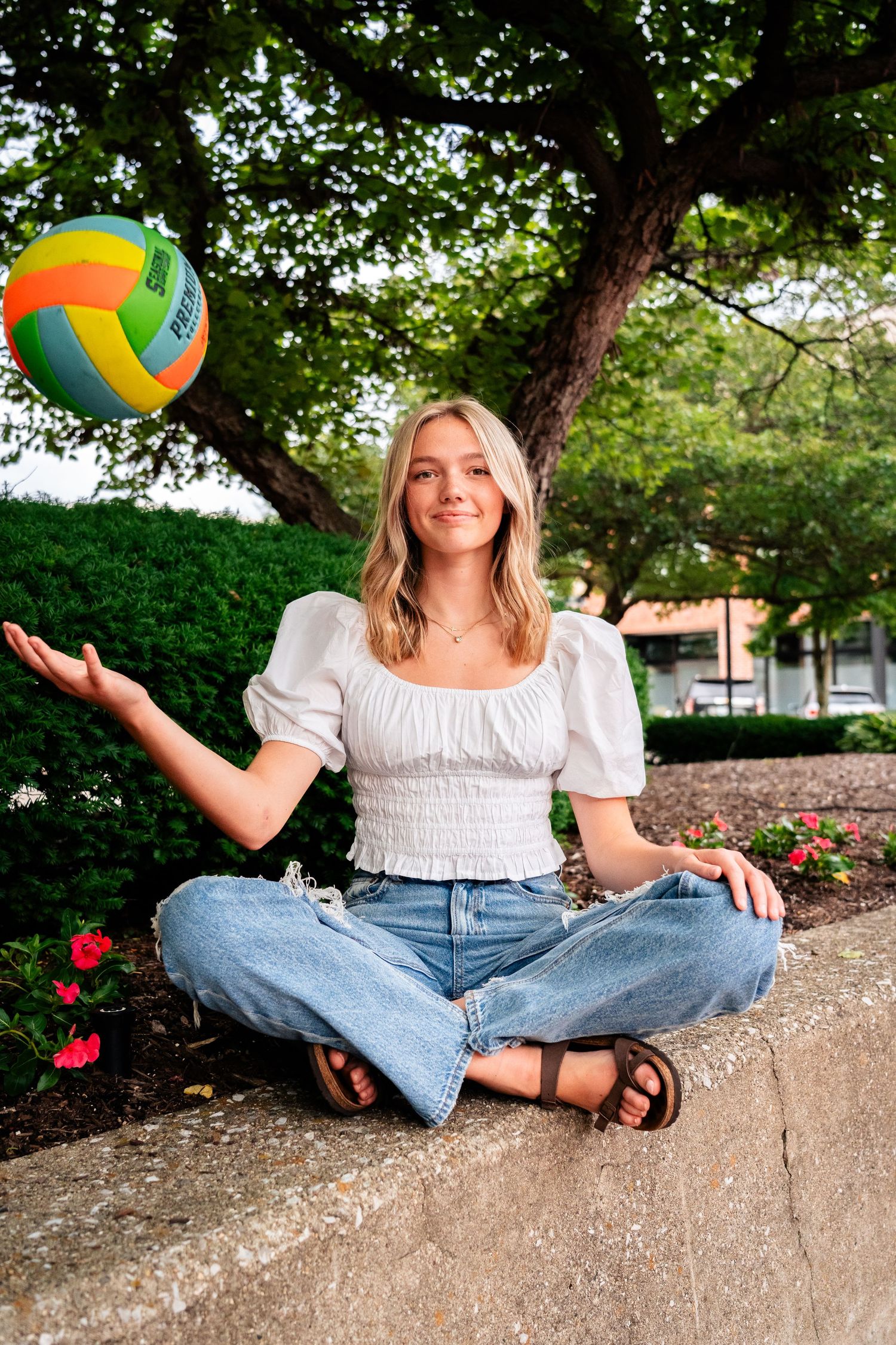 Person in white top and jeans sitting on concrete wall with colorful volleyball.