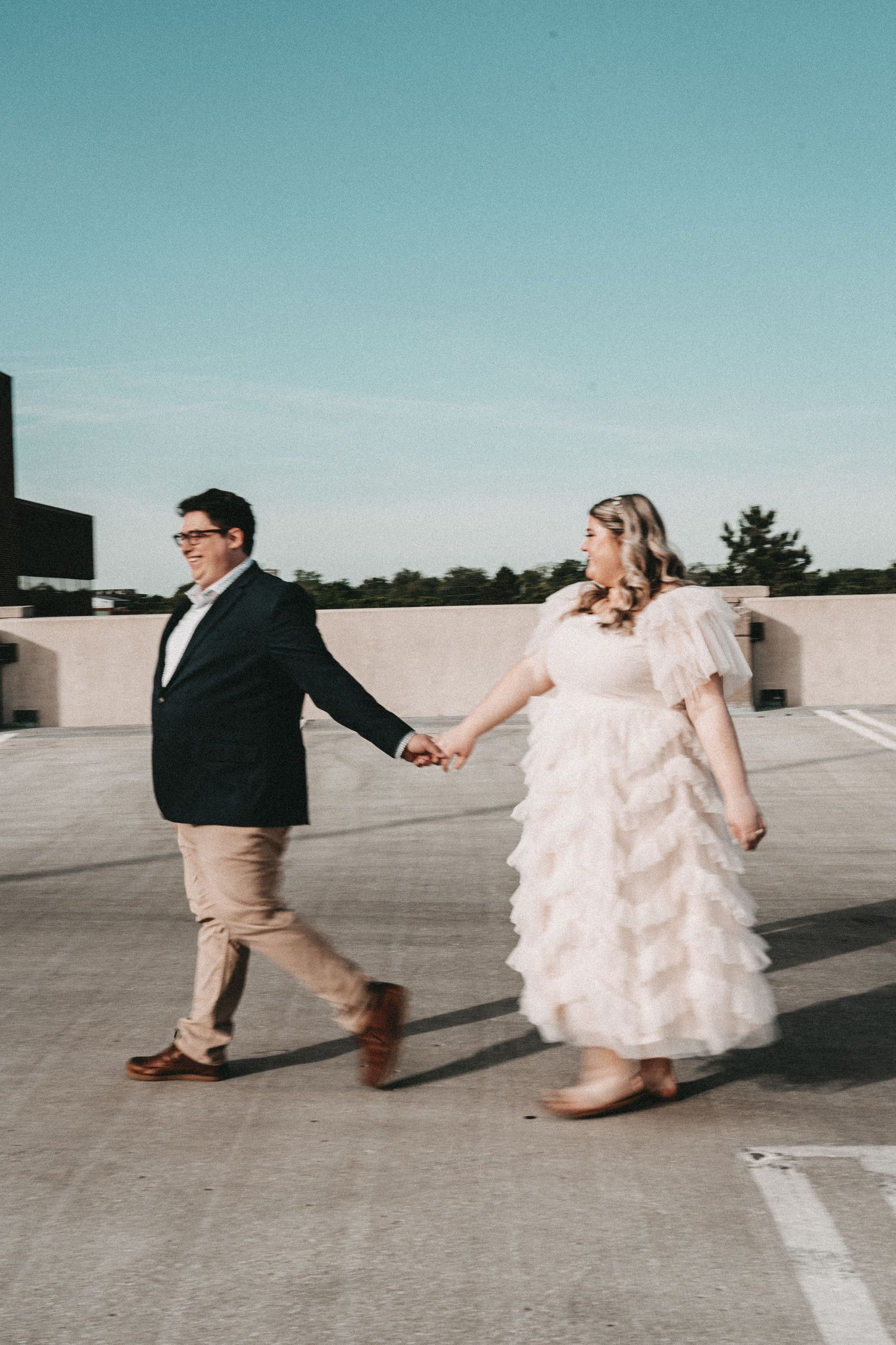 A couple dances across a rooftop in formal attire with a bright blue sky backdrop.