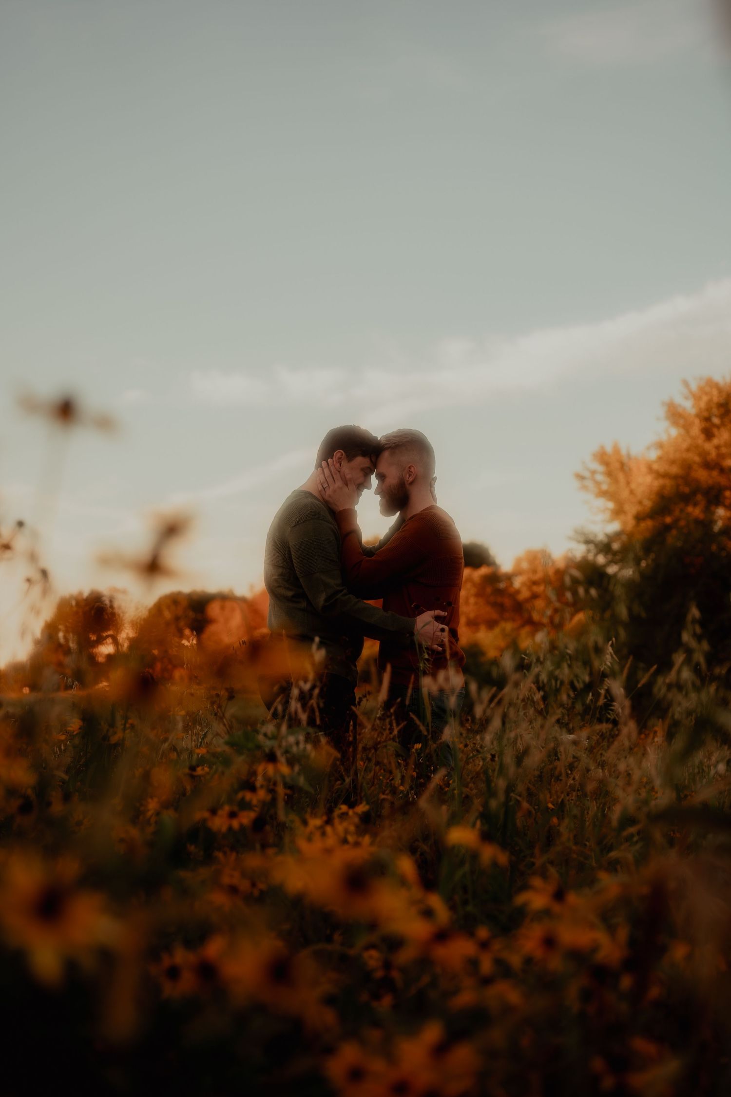 Silhouettes against a warm sunset sky in a field of tall grass and wildflowers.