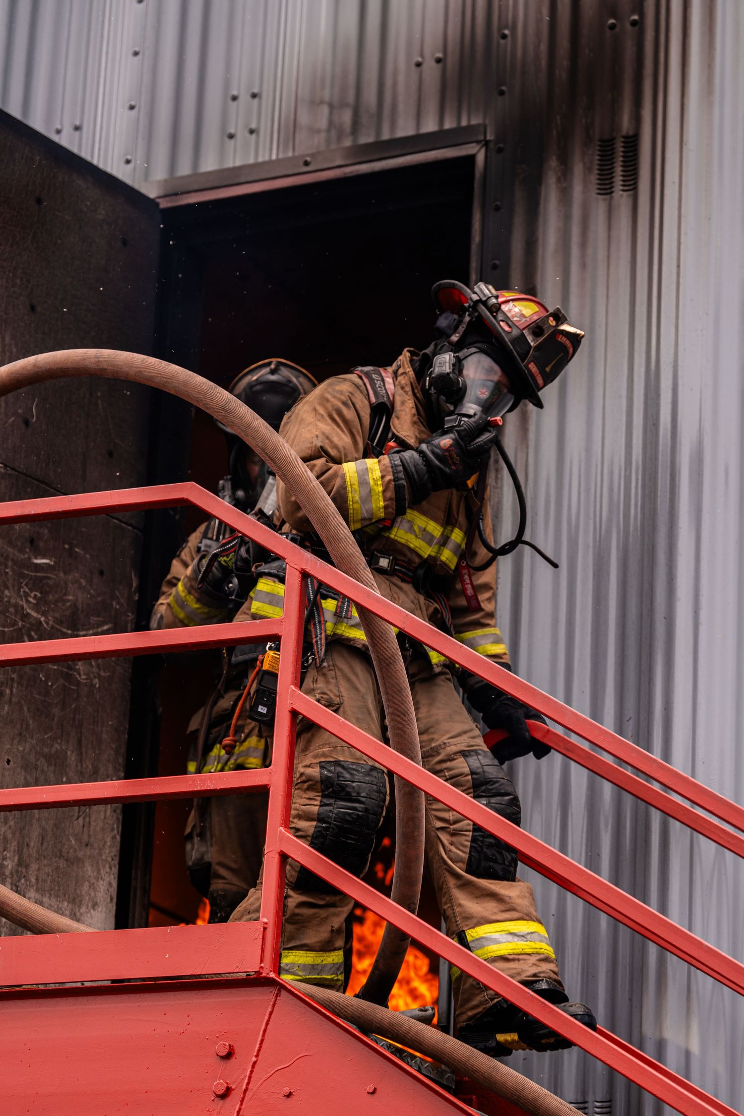 A firefighter in protective gear climbs metal stairs while handling equipment during an operation.