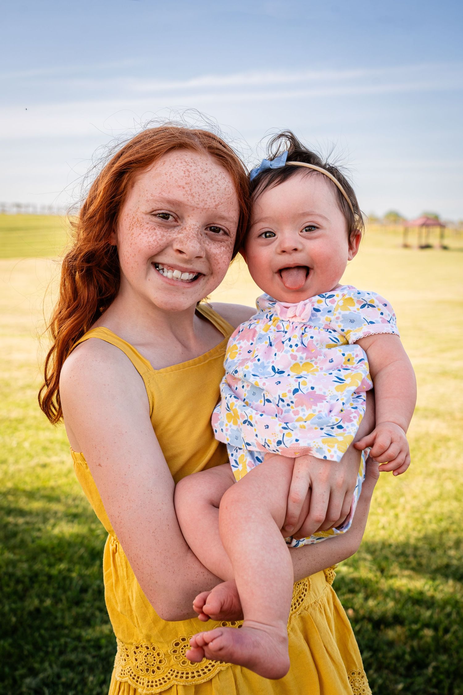 Two people share a joyful moment together in a yellow dress and floral outfit against sunny field.
