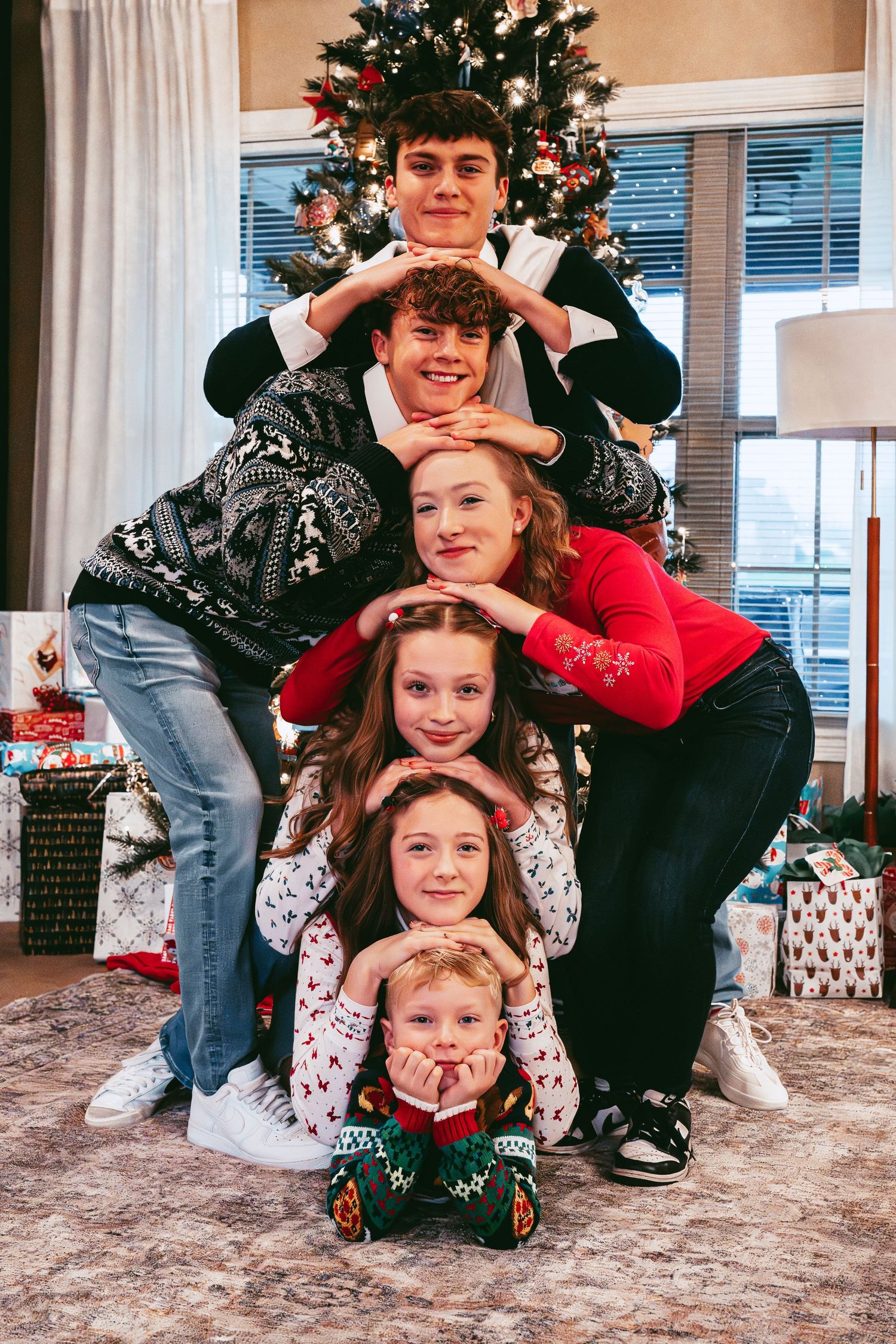 A creative holiday photo with people stacked in a pyramid formation in front of a Christmas tree.