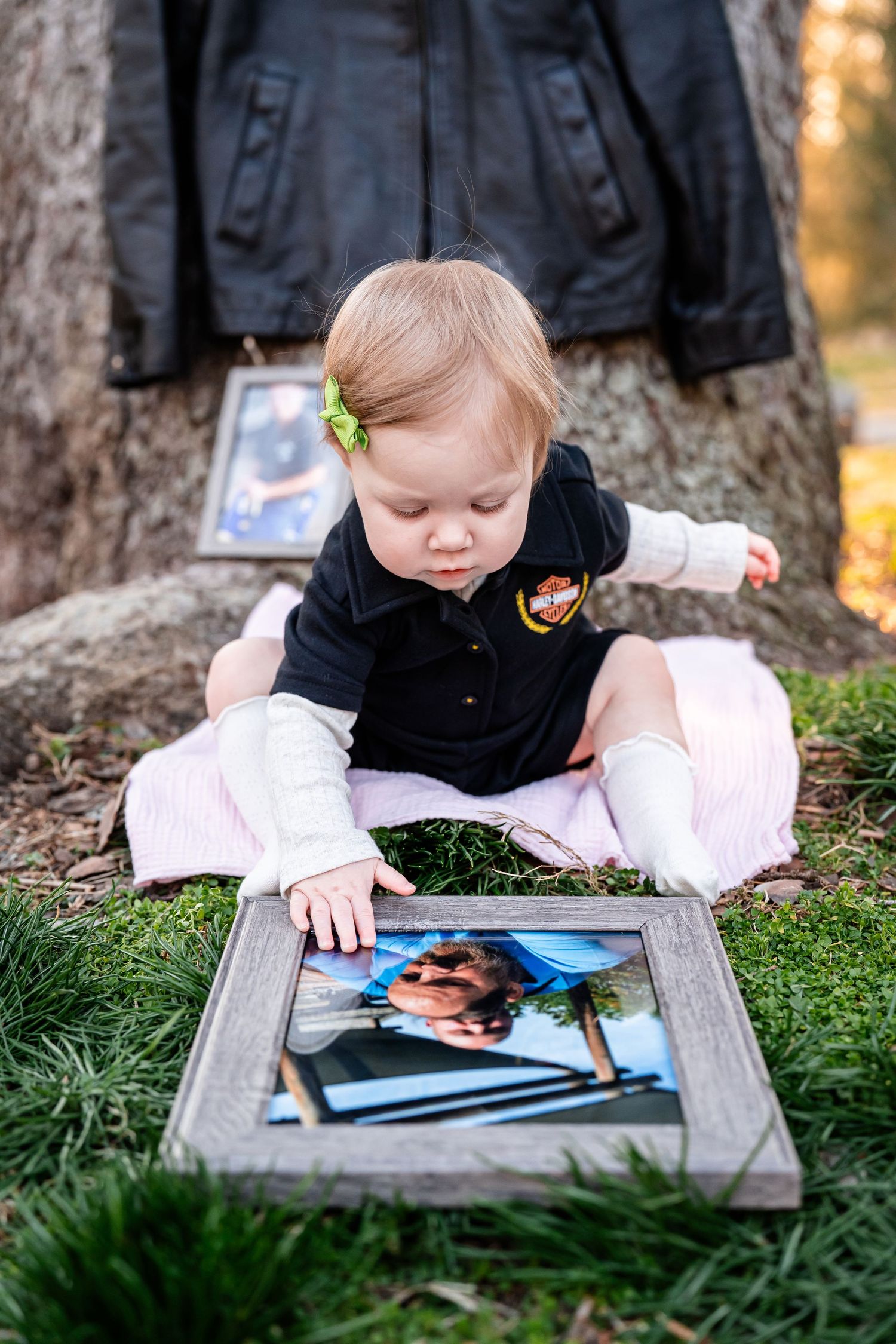 Child lying on grass looking at photos in a rustic wooden frame.