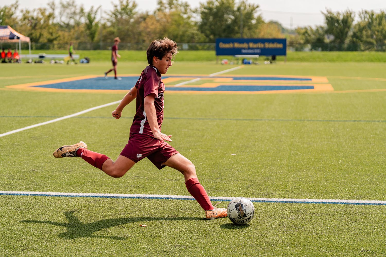 Soccer player in maroon uniform kicks ball on outdoor sports field.