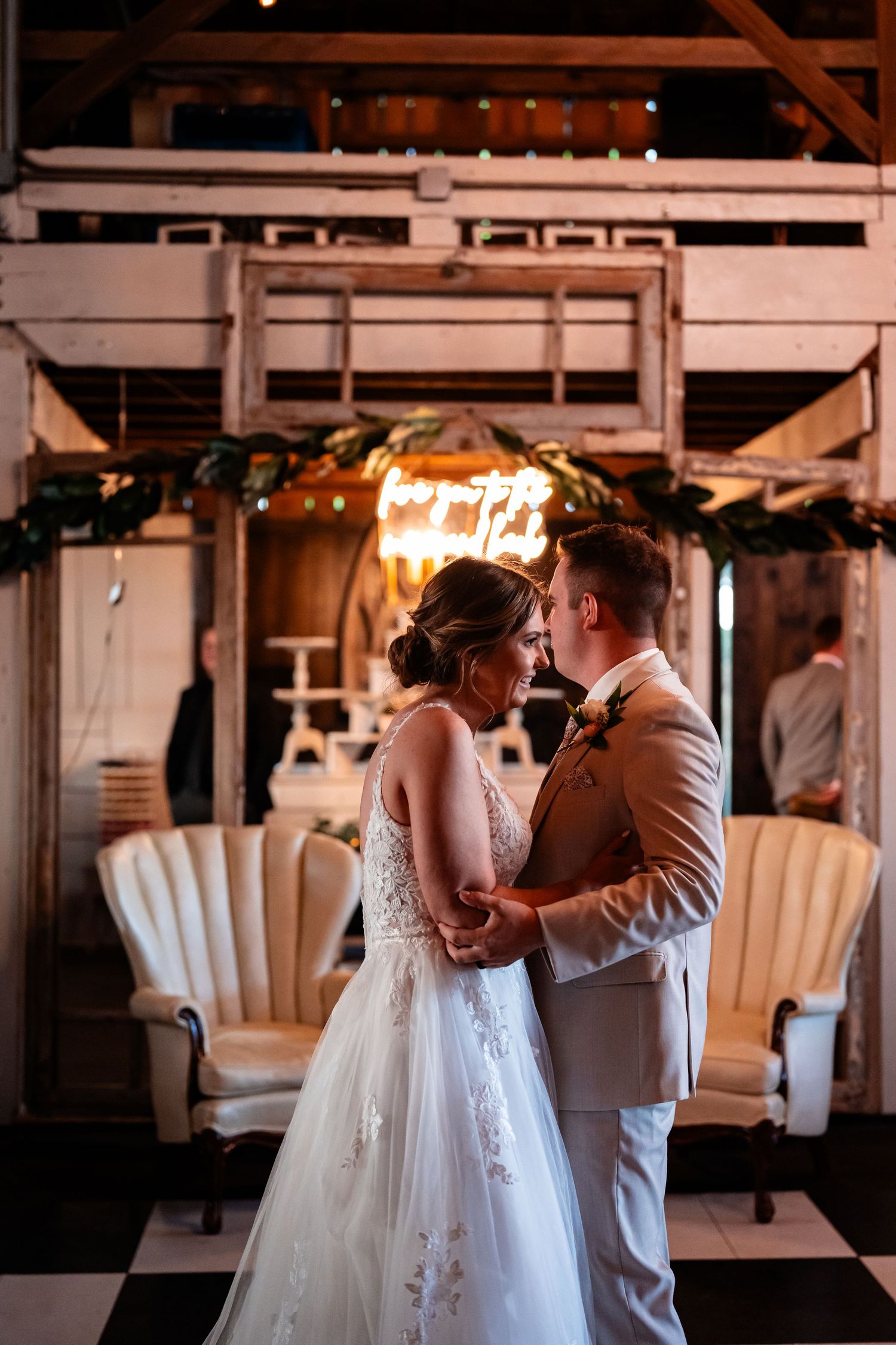 Romantic first dance between newlyweds under rustic barn lighting.