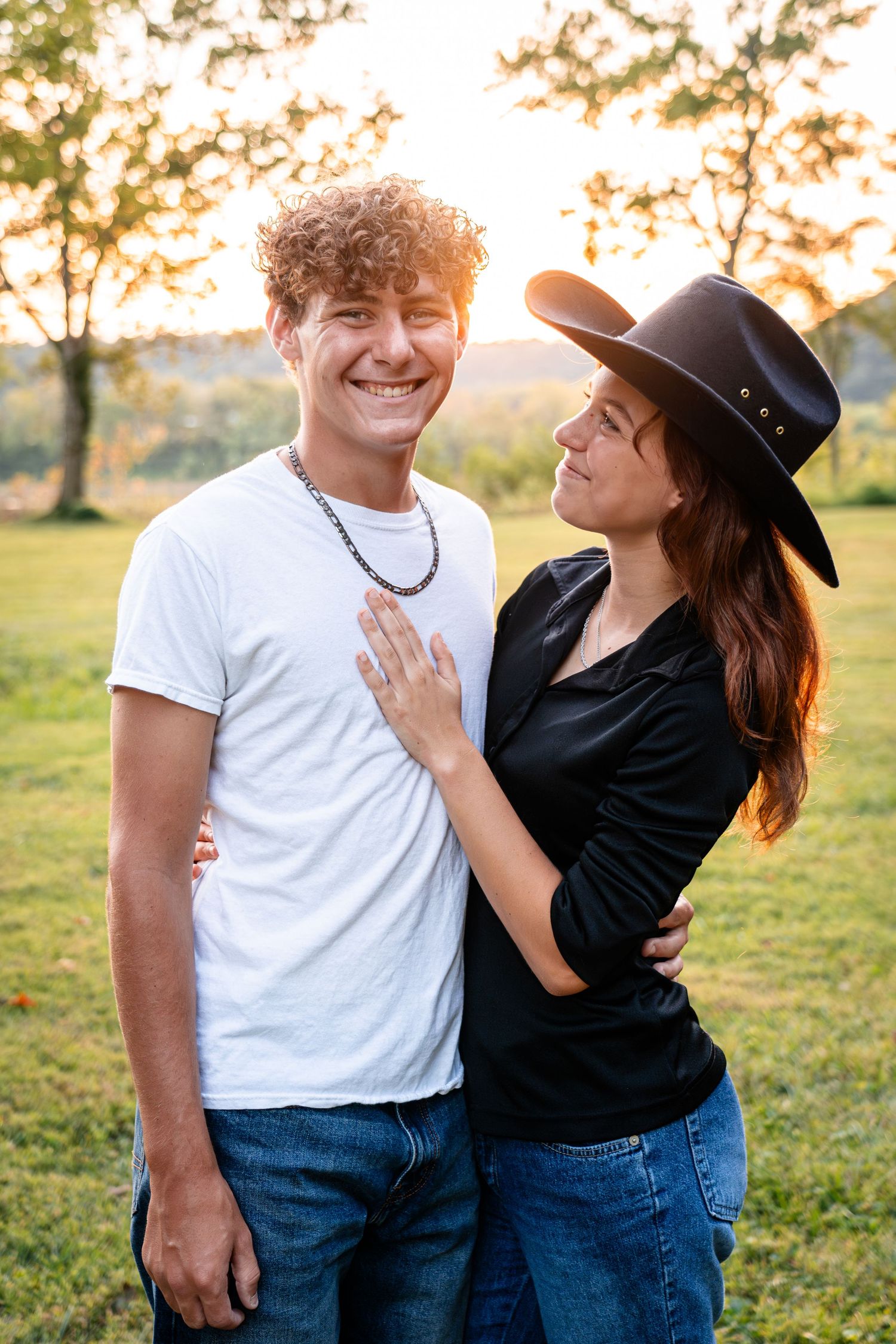 Couple in casual attire sharing joyful moments together in a sunlit field.