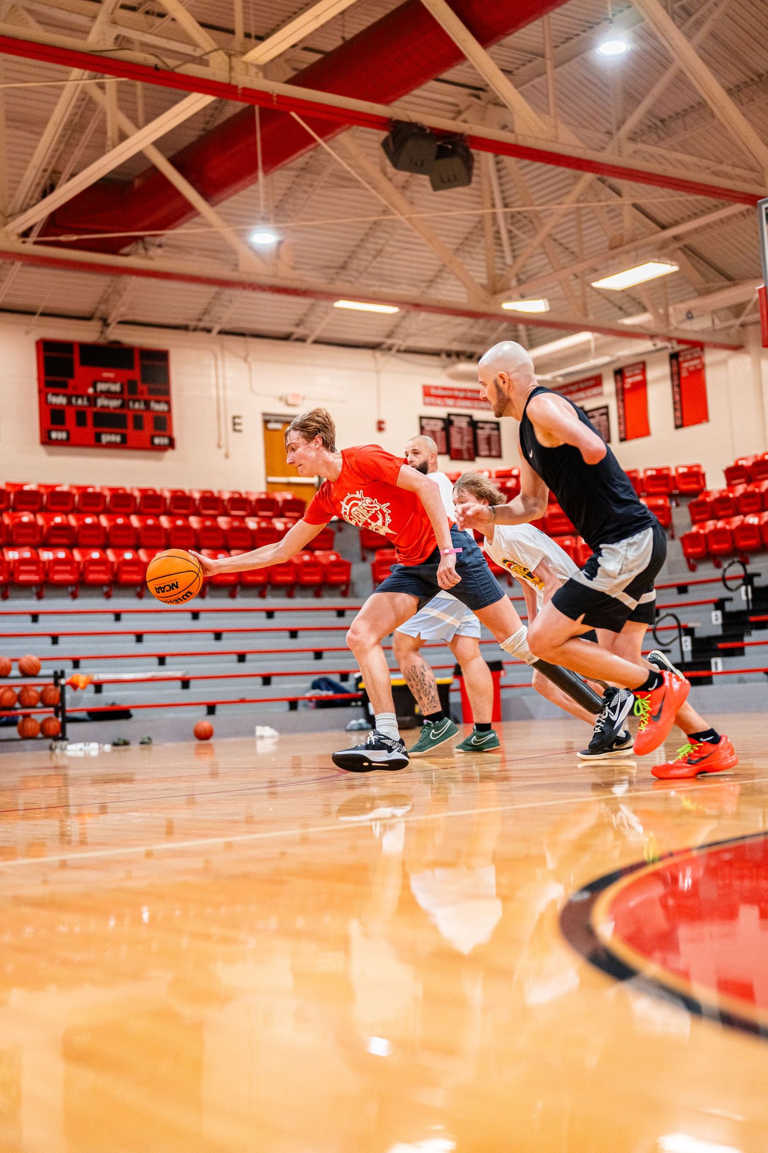 Athletes practice defensive sliding drills on a polished indoor basketball court.