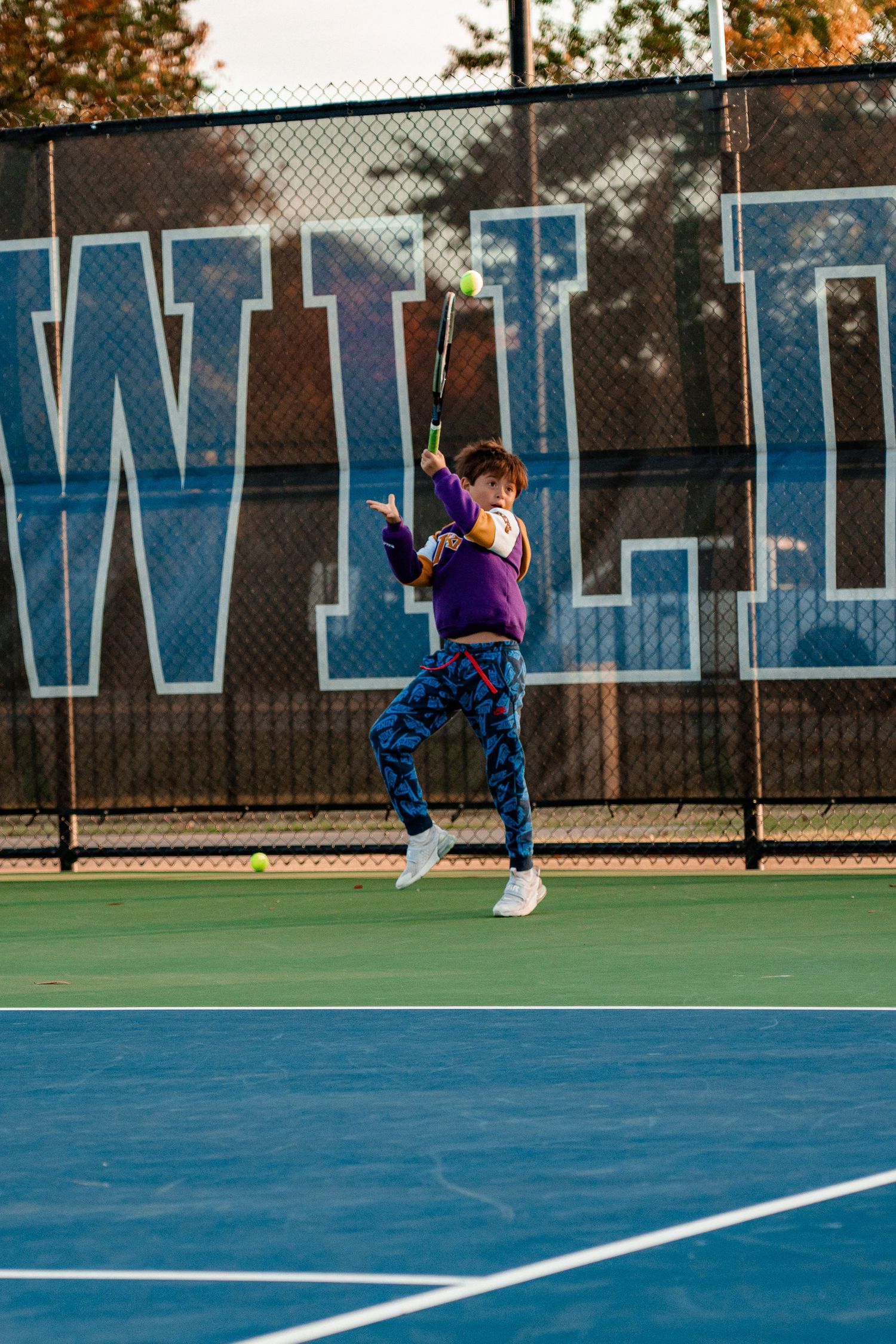 Tennis player stretches to return ball on blue outdoor court during practice session.