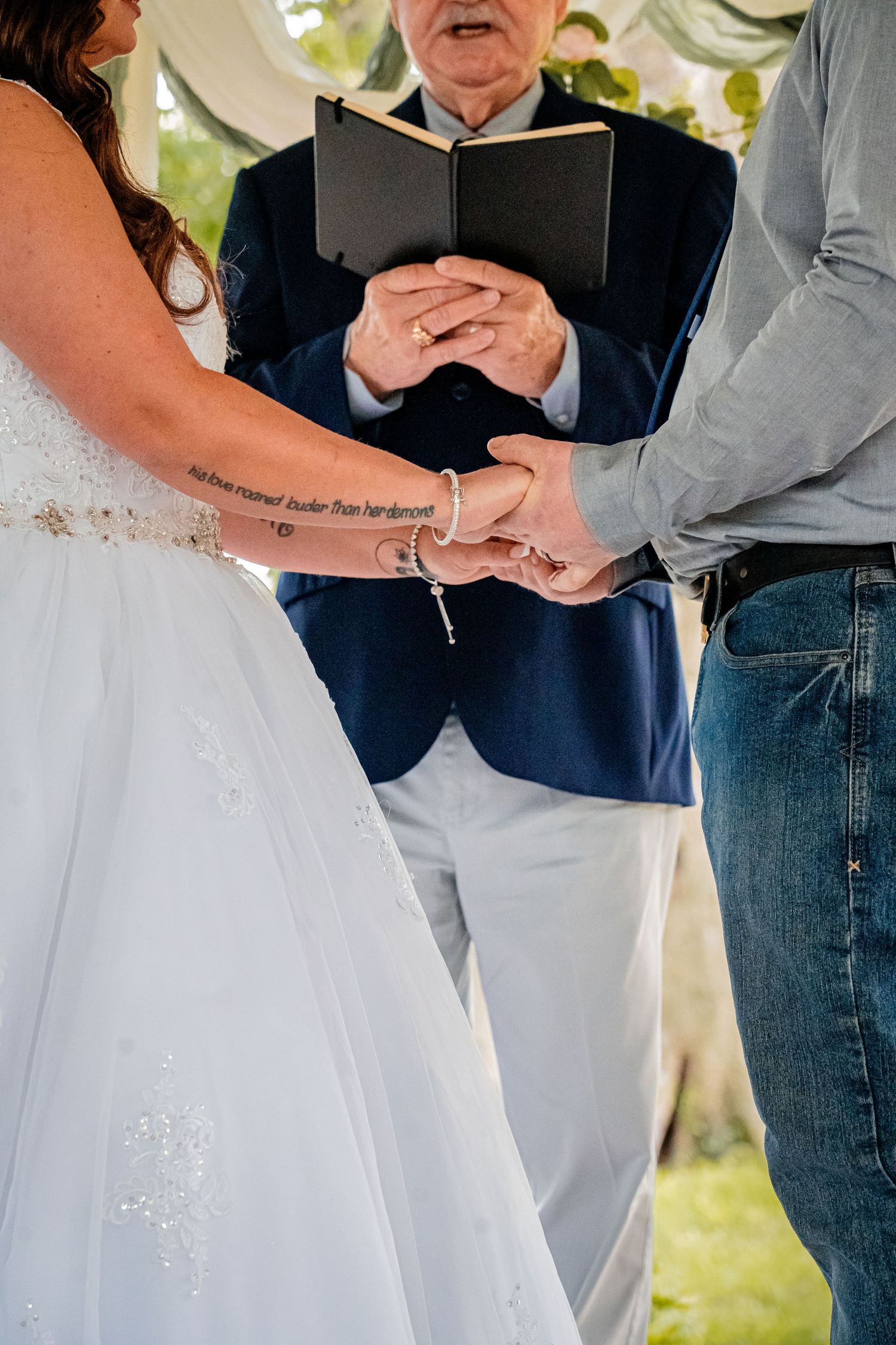 Wedding ceremony detail showing hands joined during vows with officiant holding book.