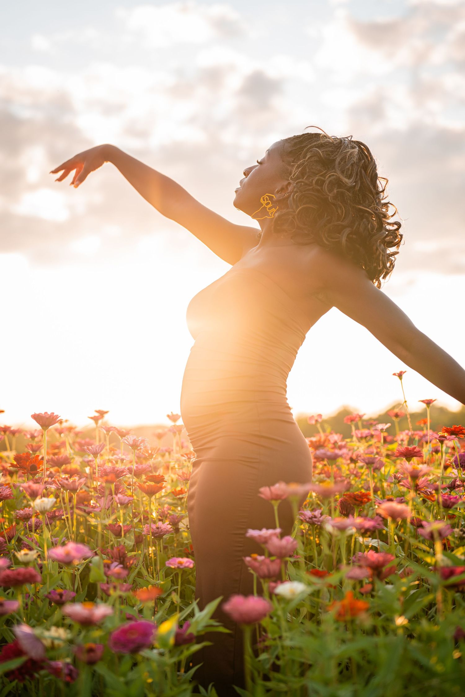 Silhouette of a pregnant woman dancing in a flower field at sunset.