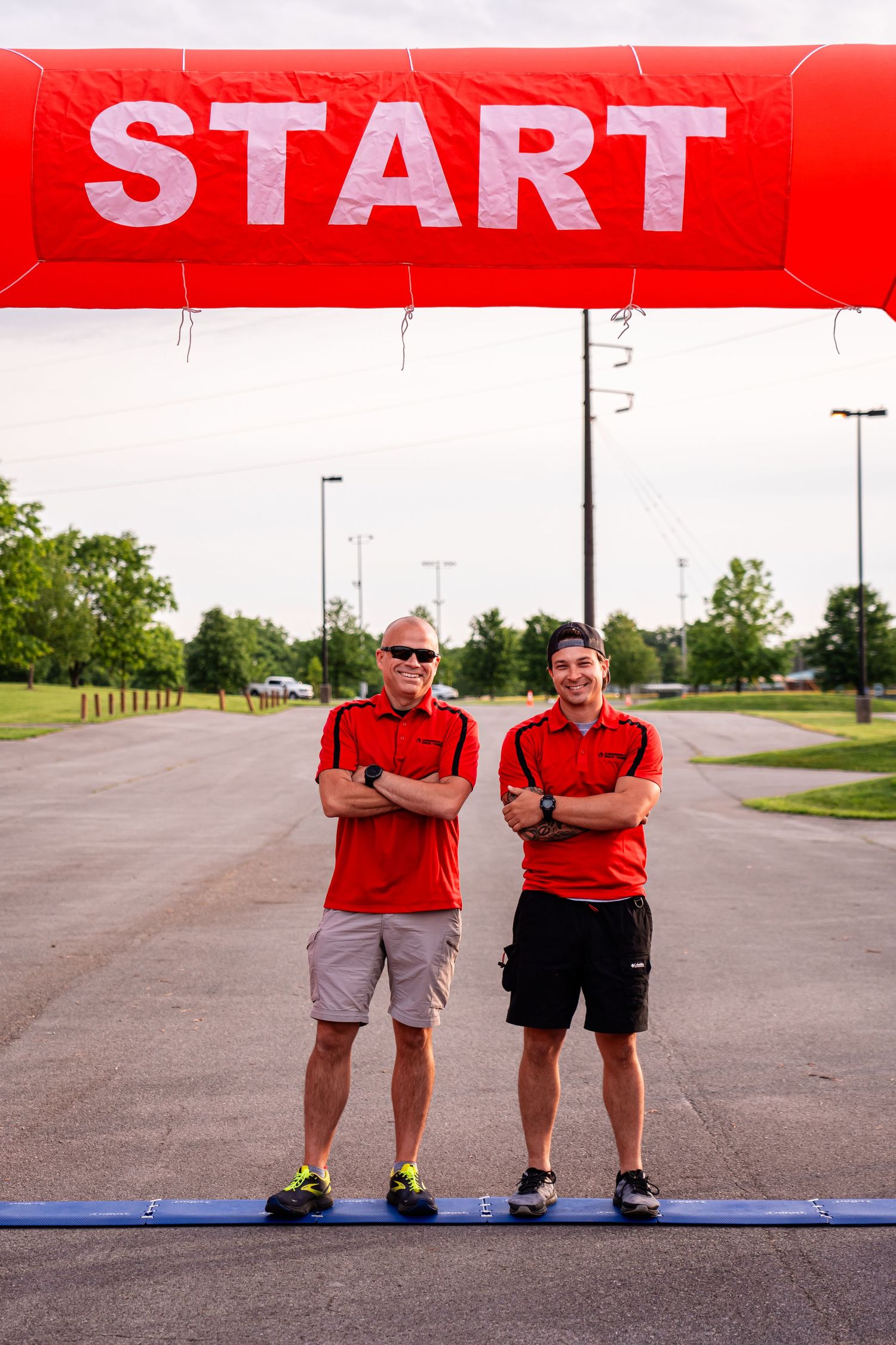 Two staff members standing under a red START banner at an outdoor event.