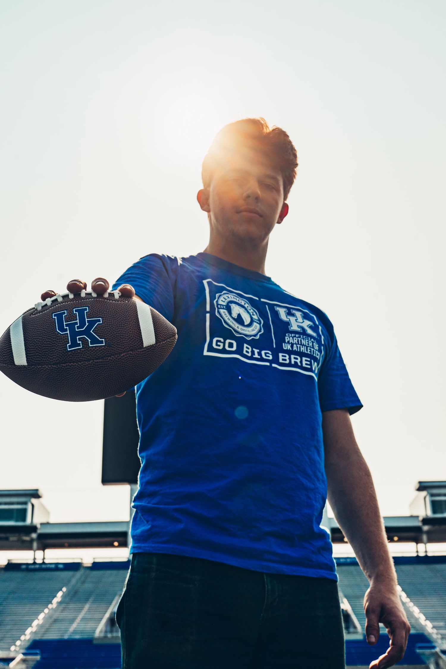 Person wearing University of Kentucky blue sports jersey against bright sky.
