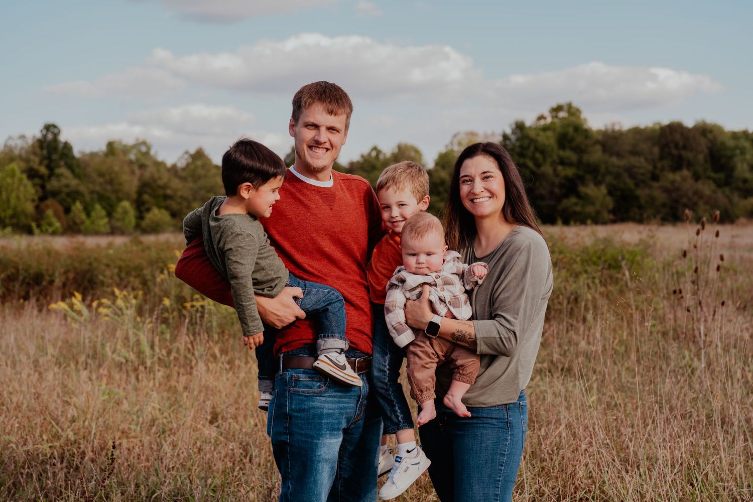 Family portrait session in a rustic field with tall grass during golden hour.