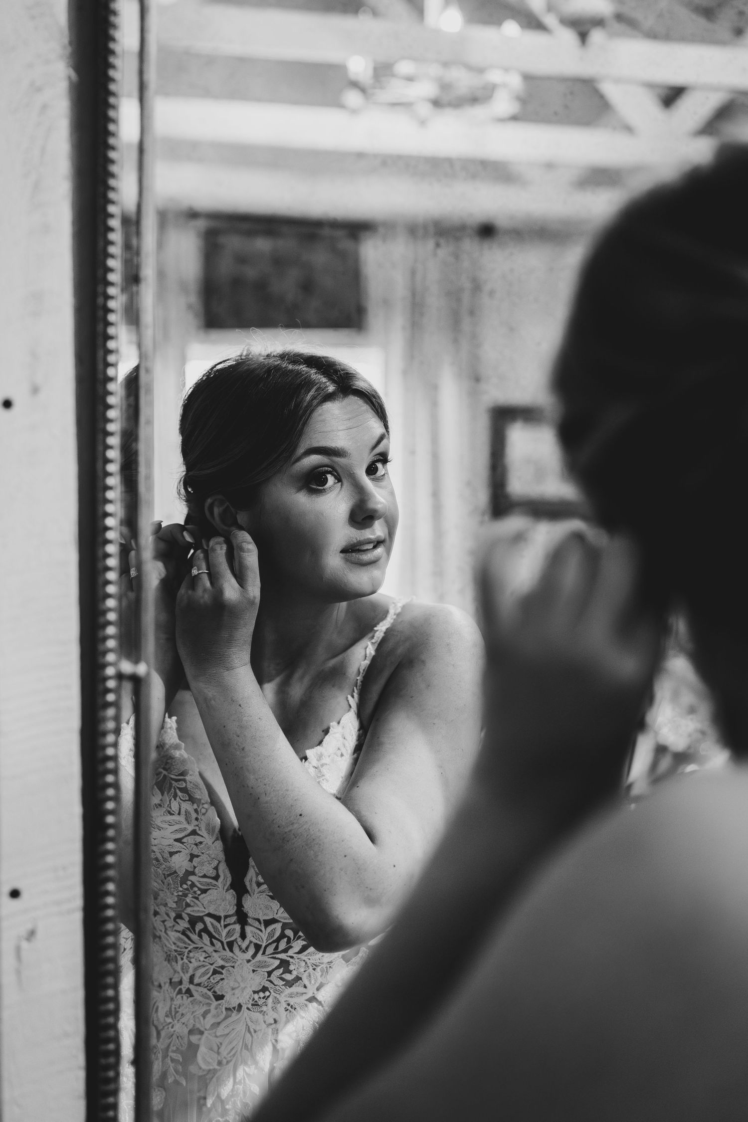 A bride applies makeup while looking in a vintage mirror during wedding preparations.