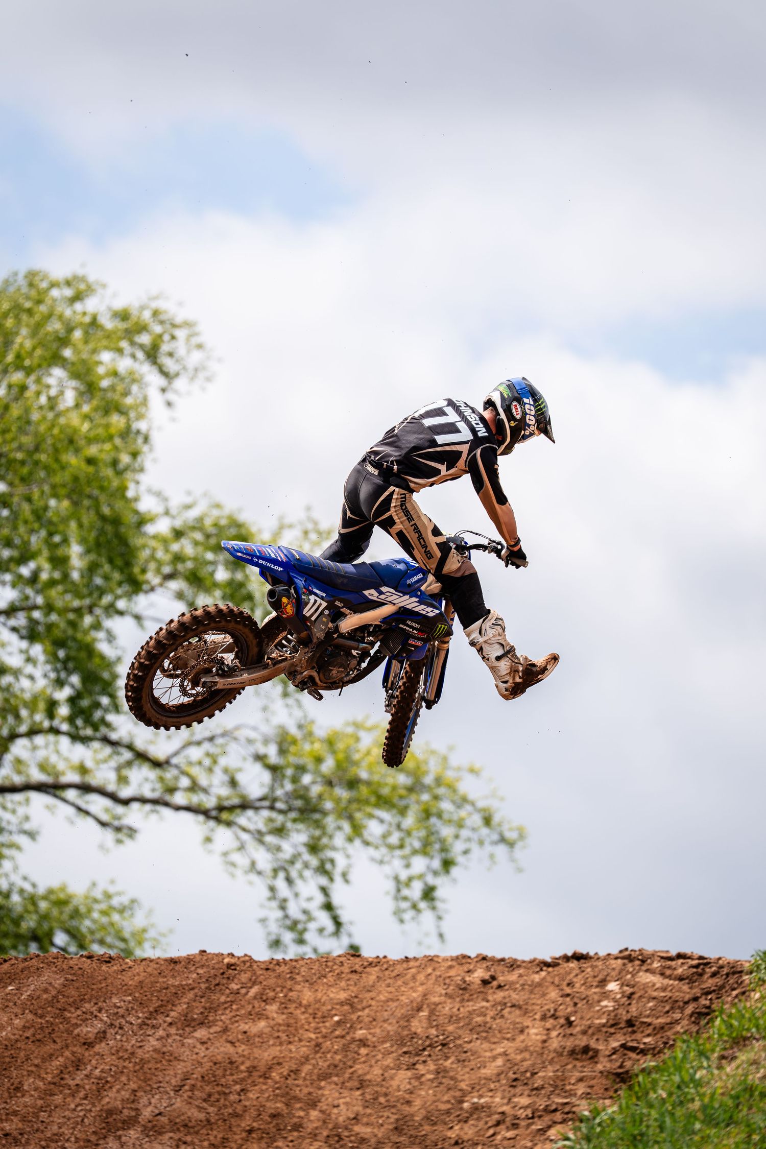 Motocross rider performs impressive aerial jumps and tricks over dirt mounds.