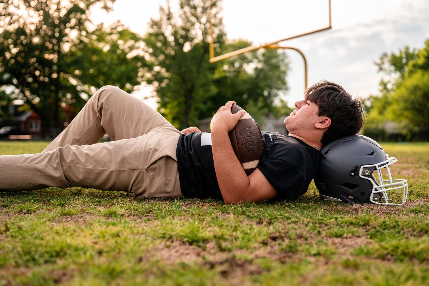 Football player lying on grass field during golden hour photo session.